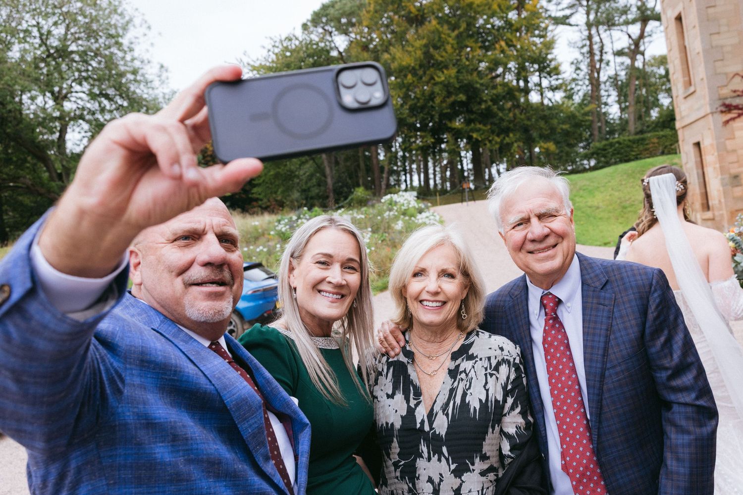 Group of wedding guests taking selfies outdoors on a sunny day.