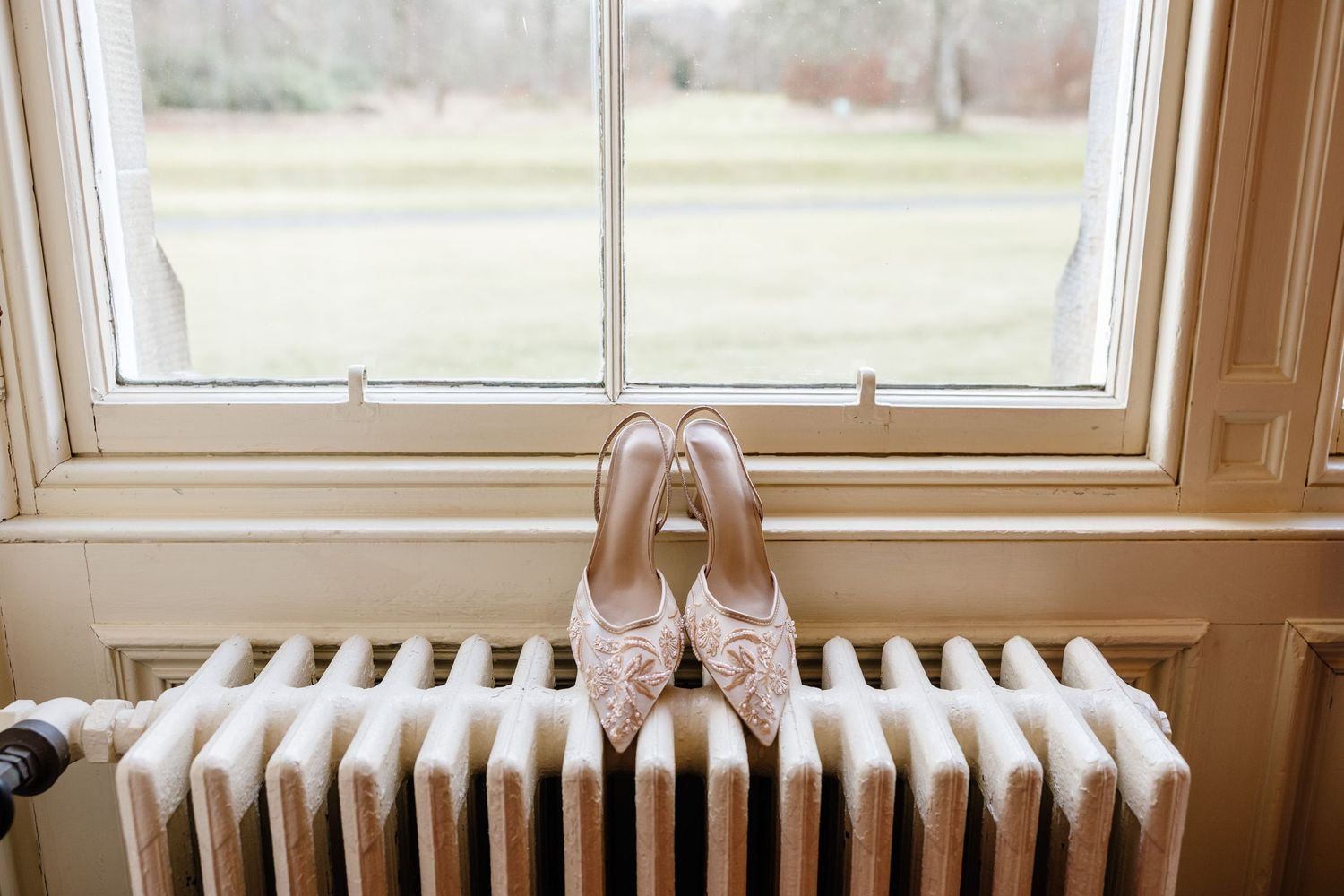 A vintage-style radiator sits beneath a window in a room with warm wood trim and natural light.