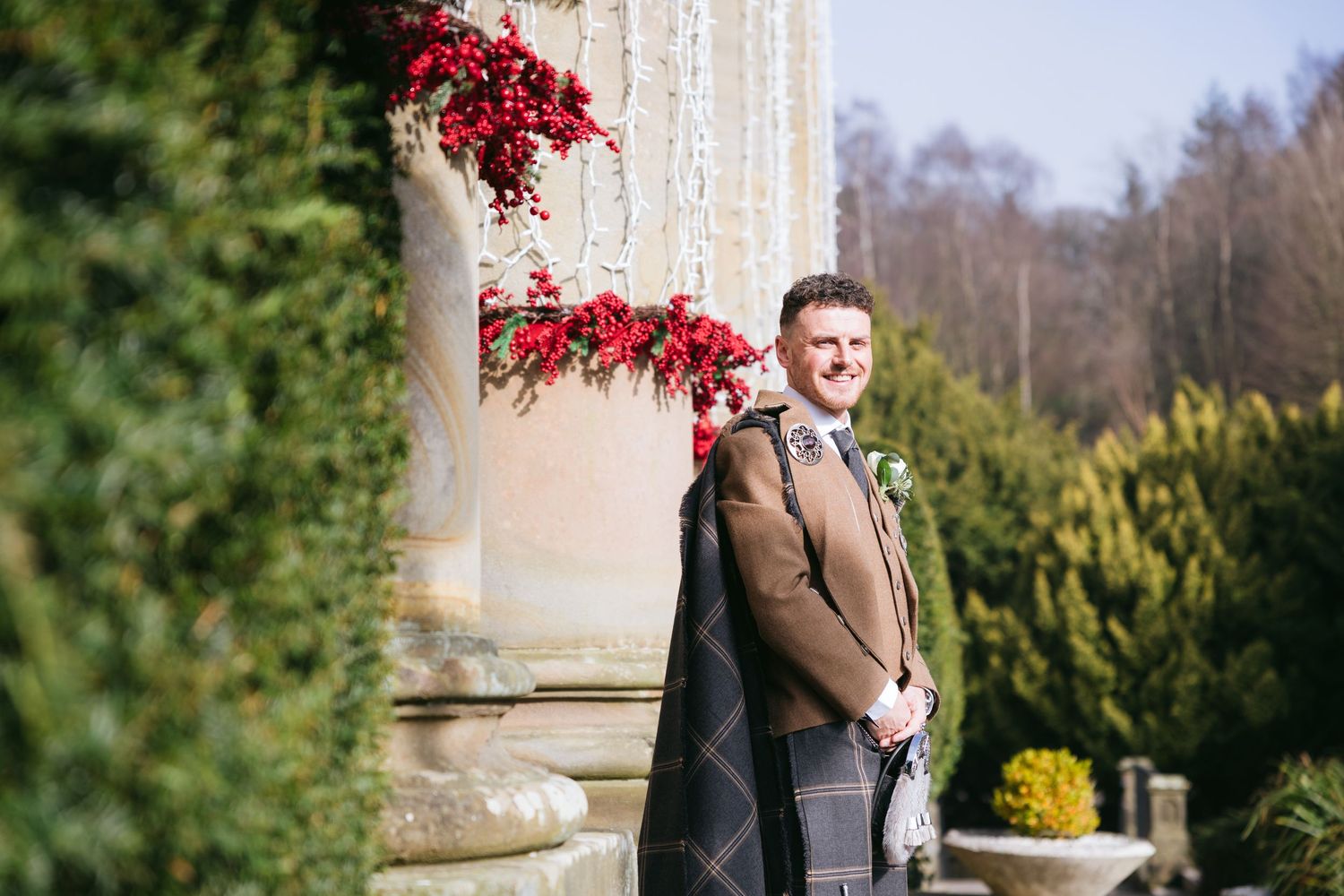 Wedding couple shares tender moment beneath cascading red flowers in a garden setting during autumn.