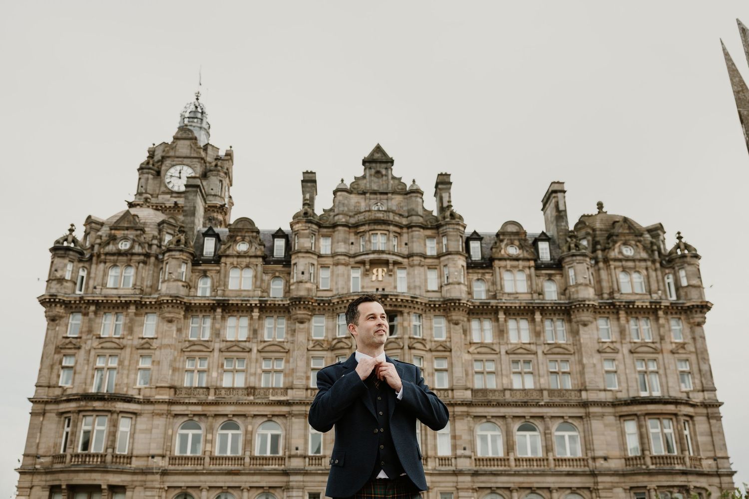 Figure in dark attire stands in front of the ornate facade of Edinburgh's Balmoral Hotel in Scotland.
