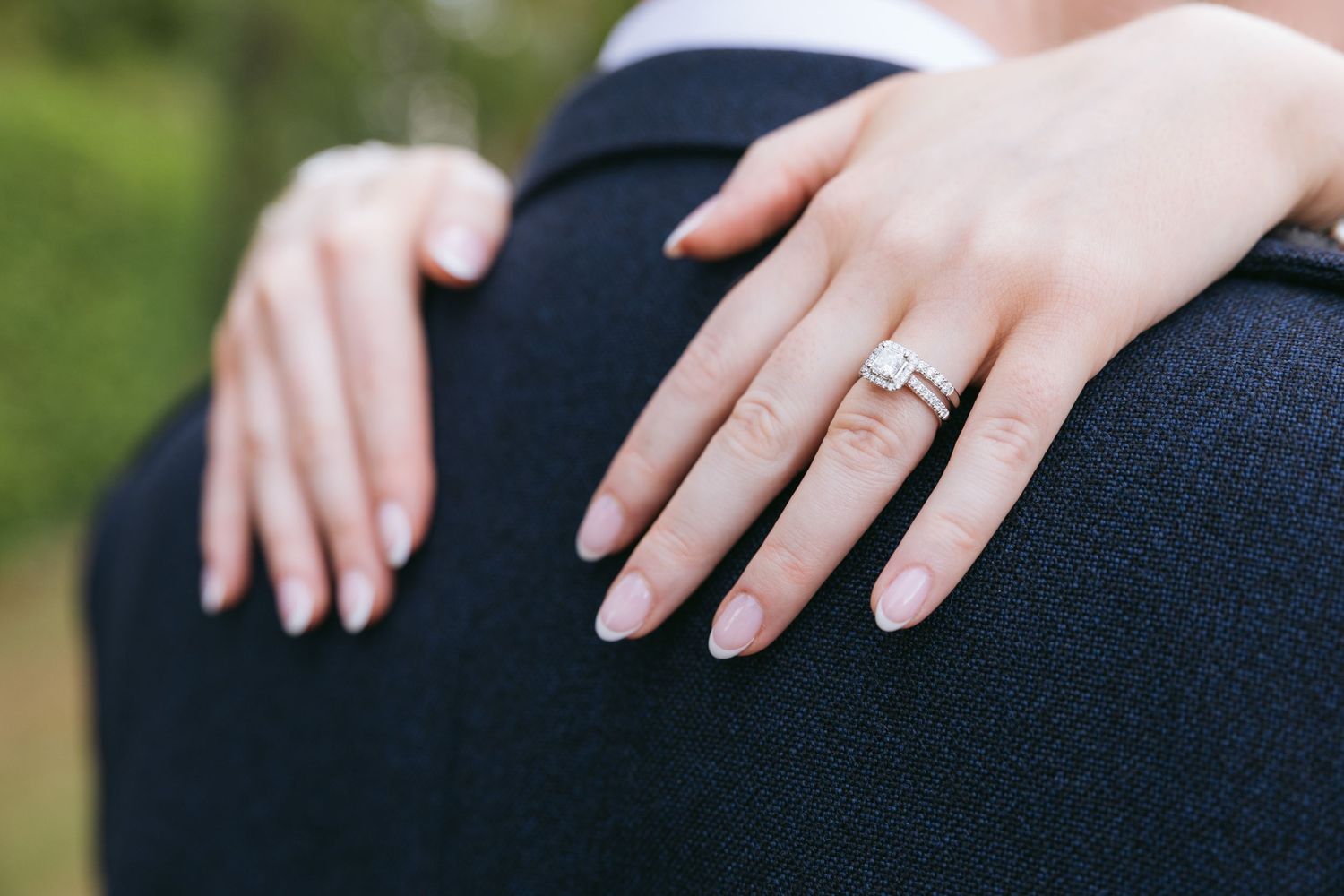 Close-up view of wedding rings on hands against dark fabric background shows elegant engagement and wedding bands.