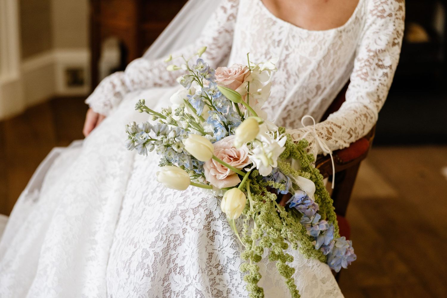 A delicate white lace wedding dress with long sleeves and floral details hangs elegantly against a dark background.
