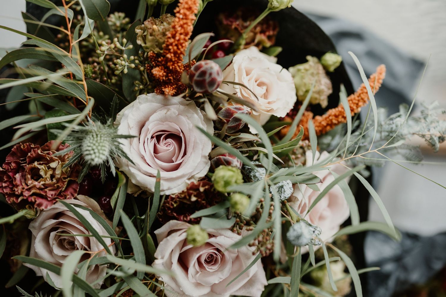 Wedding bouquet with blush pink roses, orange accents, and greenery in a romantic rustic style.