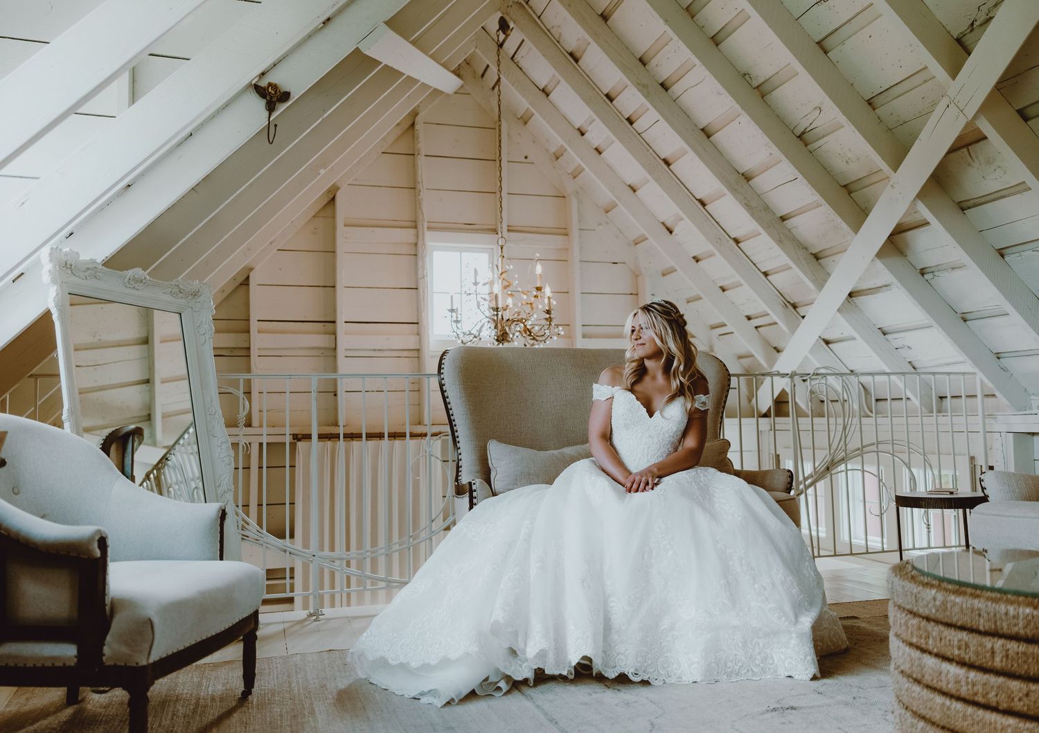 A white wedding dress flows elegantly in an airy attic space with white beams and rustic furnishings.