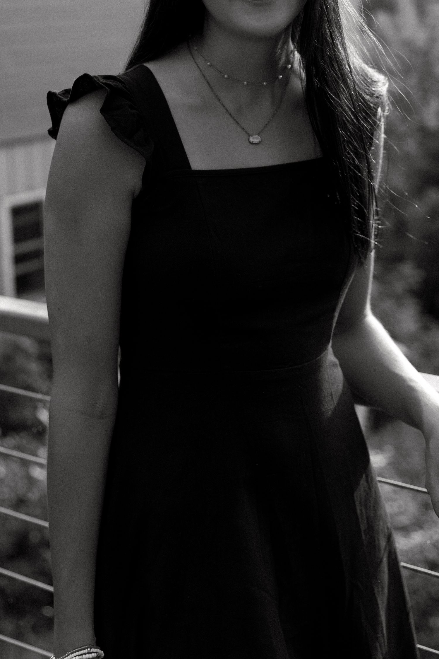 Black and white photo showing details of a formal dress with ruffle sleeves and delicate necklace accessories.
