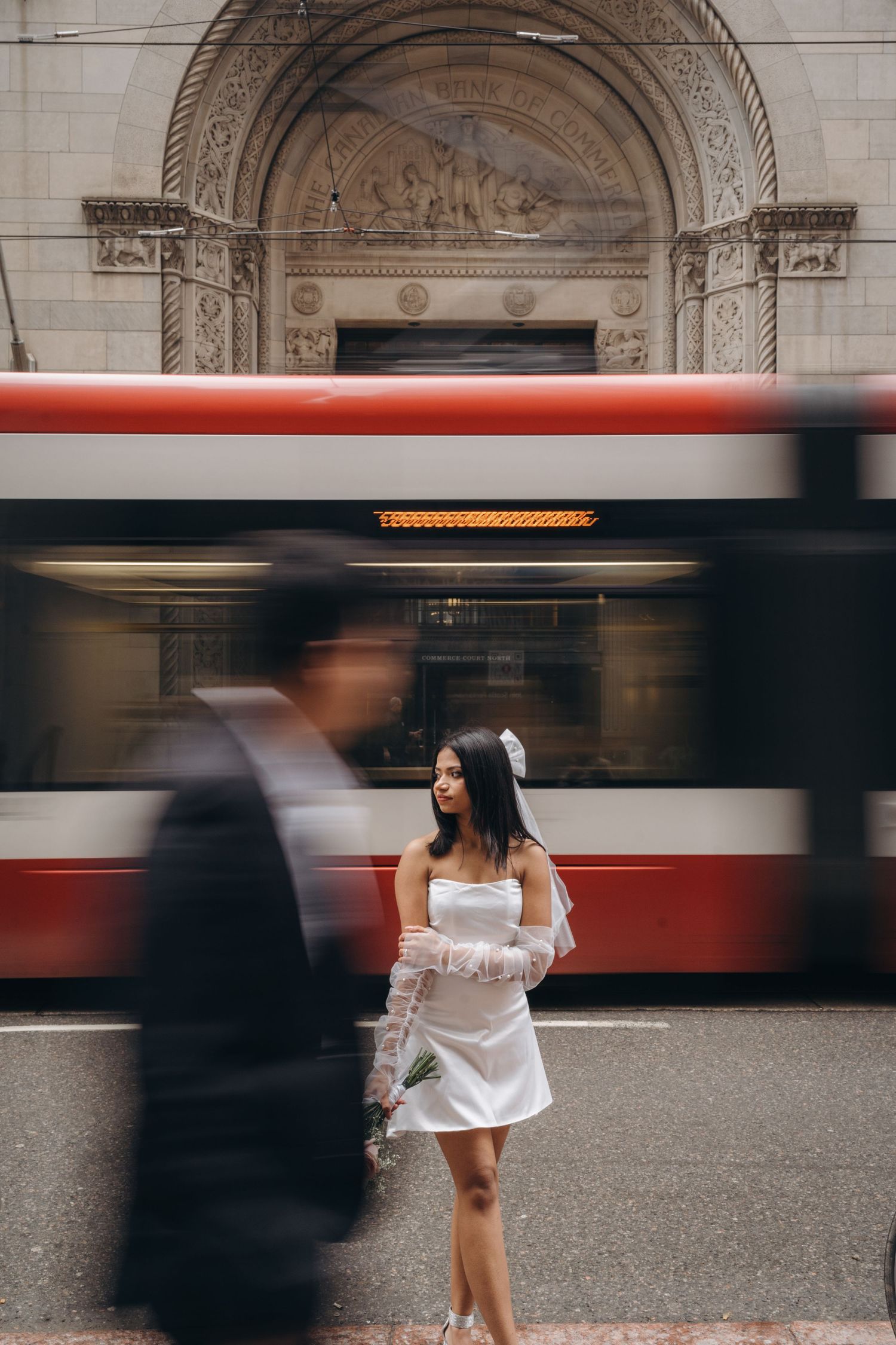 A streetcar blurs past ornate architectural details while a person in white stands on the platform.