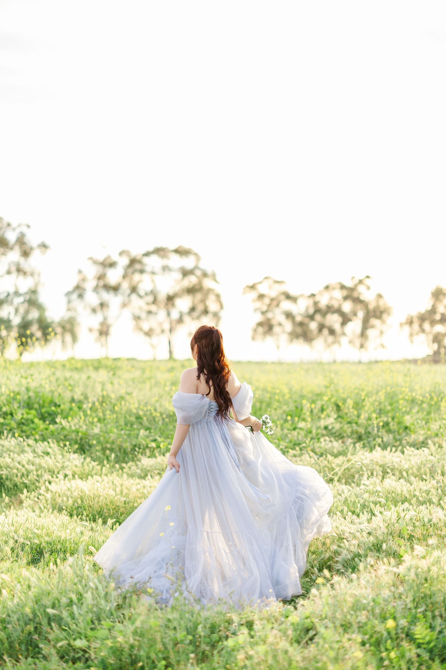 A person in a flowing white dress twirls gracefully in a sunlit meadow during golden hour.