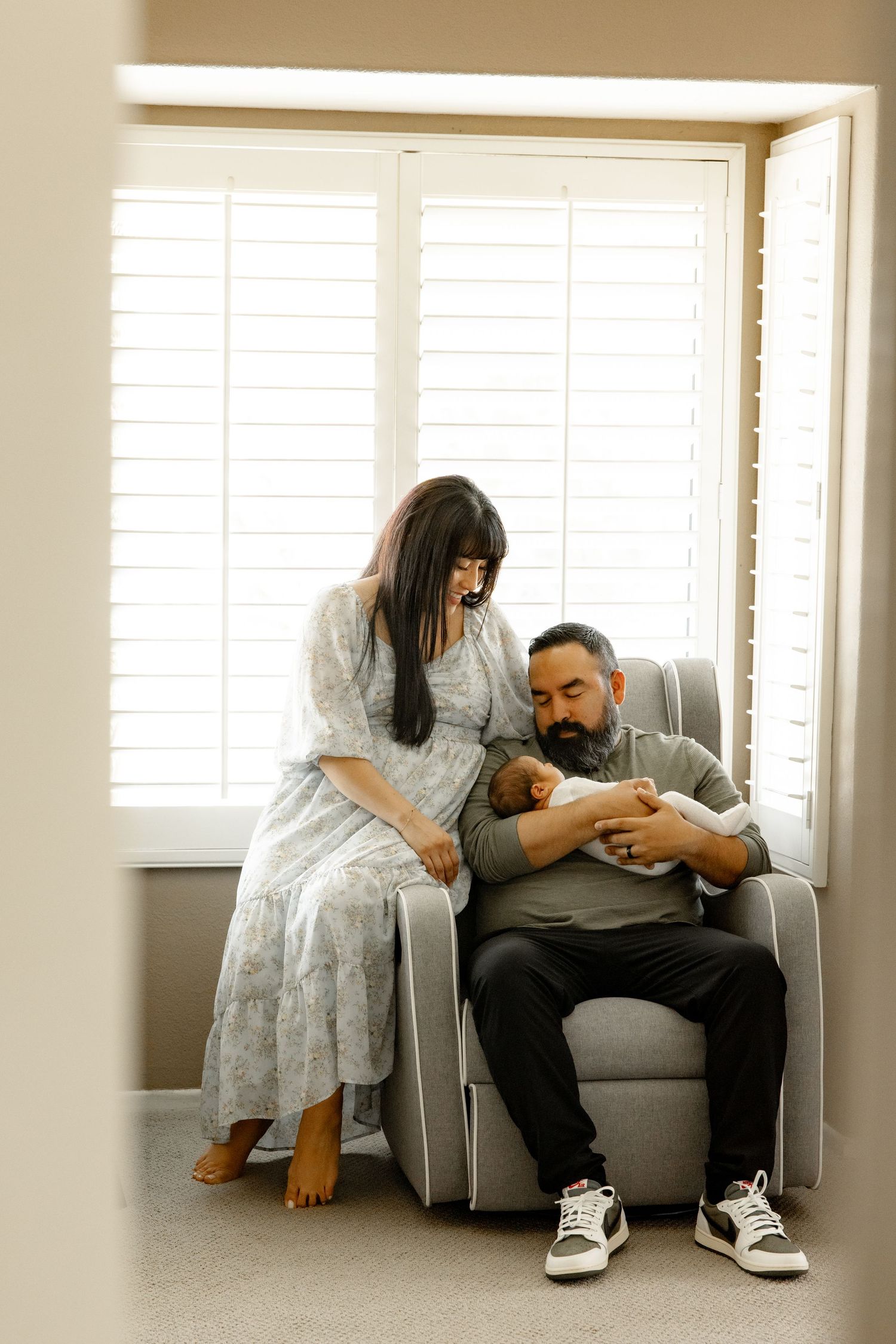An intimate indoor maternity moment captured in a cozy armchair by a bright window.
