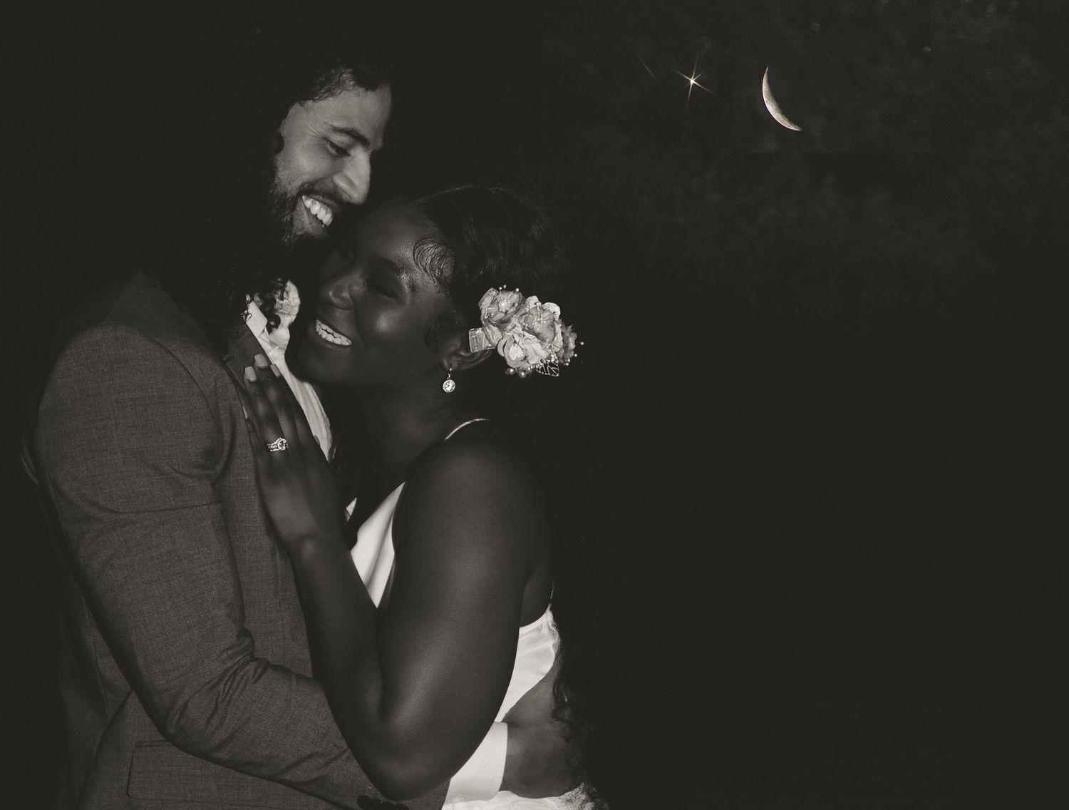 A romantic black and white portrait of a couple under a crescent moon.