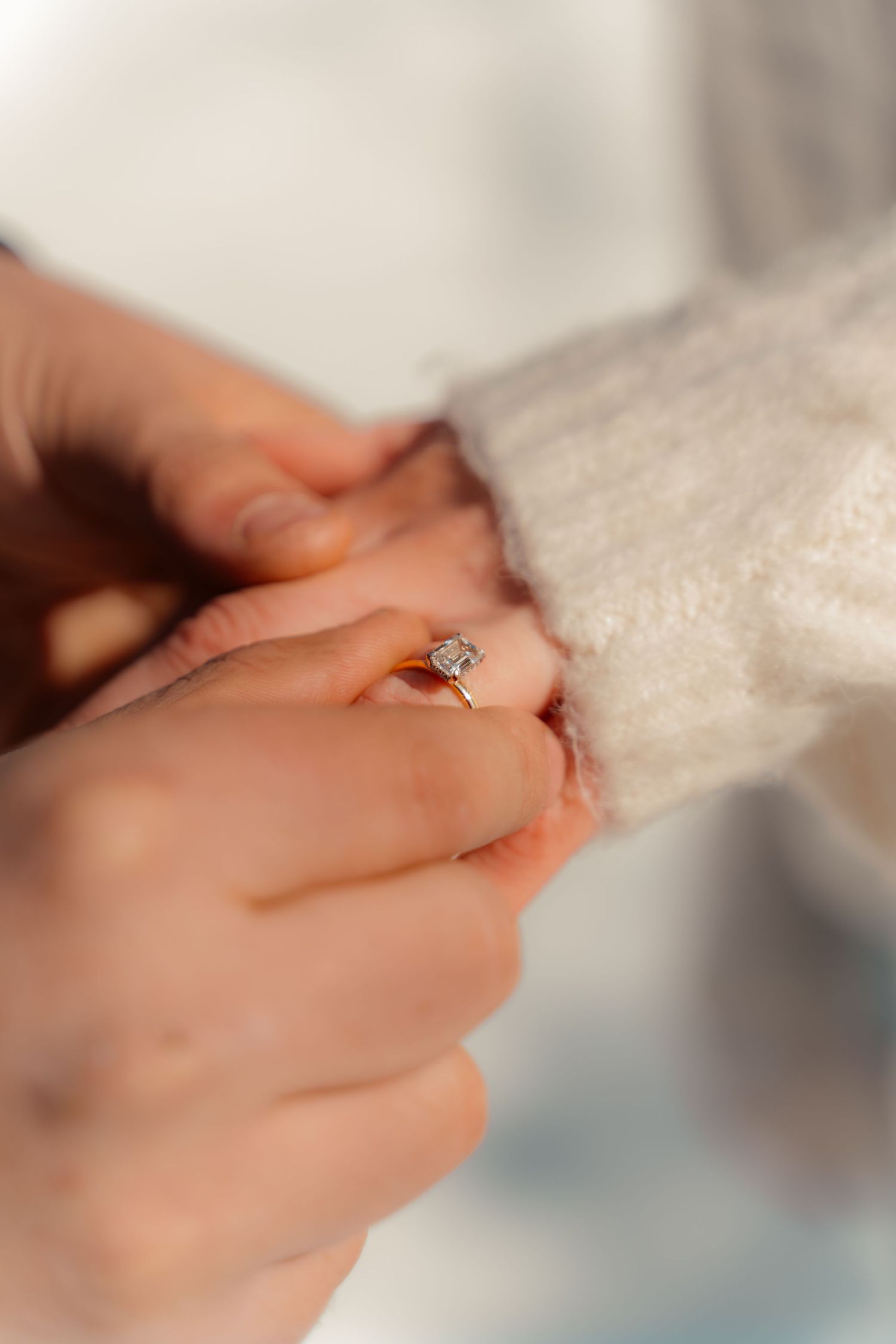 Close-up of a delicate engagement ring with white lace sleeve in soft natural lighting.
