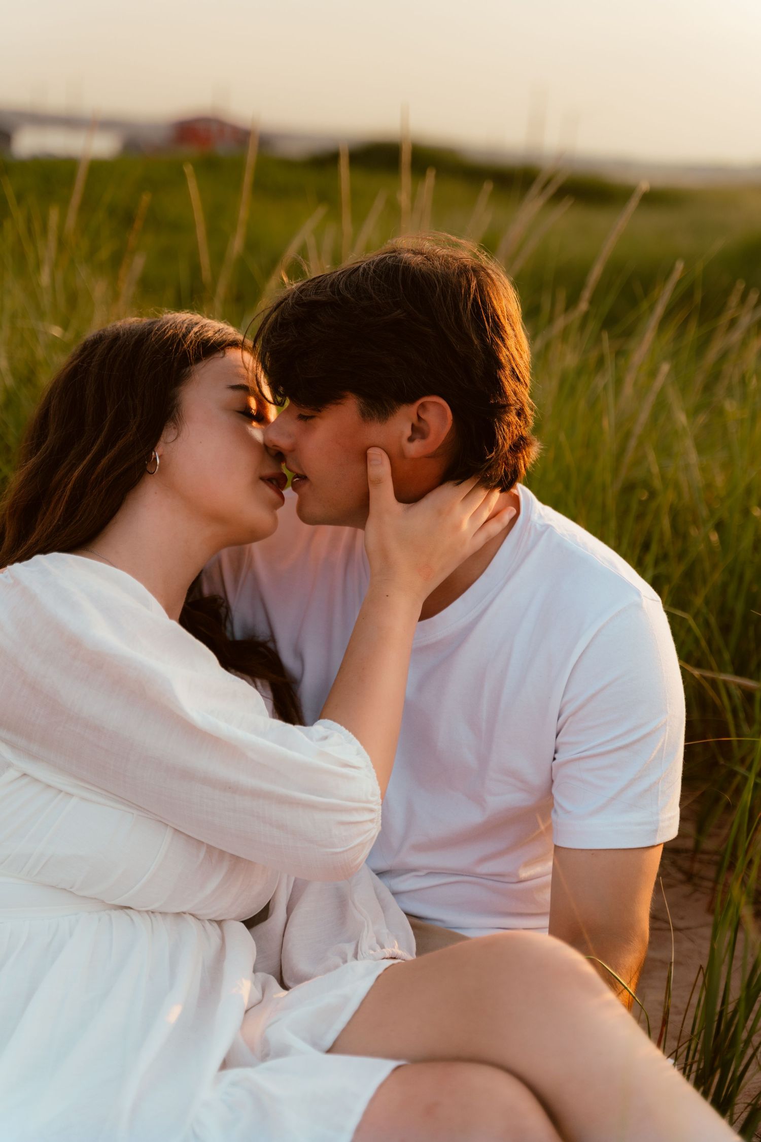 Romantic couple sharing an intimate moment in a sunlit meadow with tall grass at sunset.