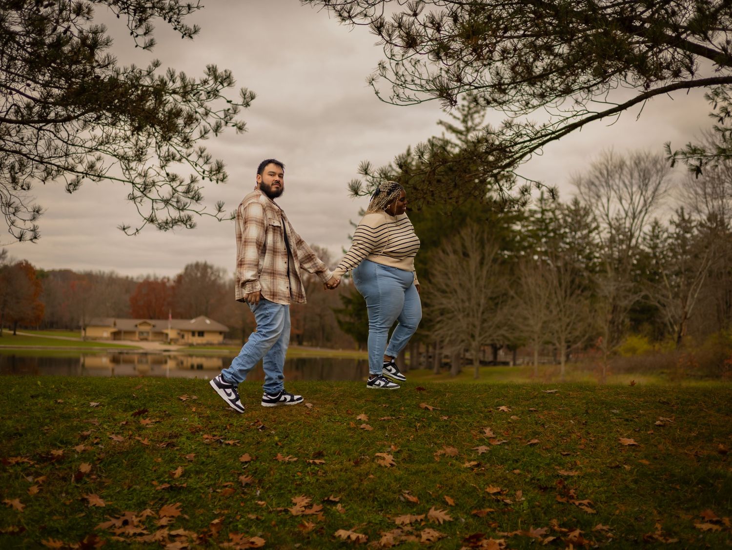 A couple playing with their child on a grassy hillside on an autumn afternoon as fallen leaves scatter around them.