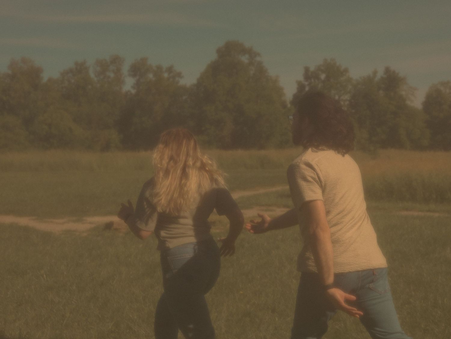 Two people dancing together in a golden-lit meadow with trees in the background at sunset.