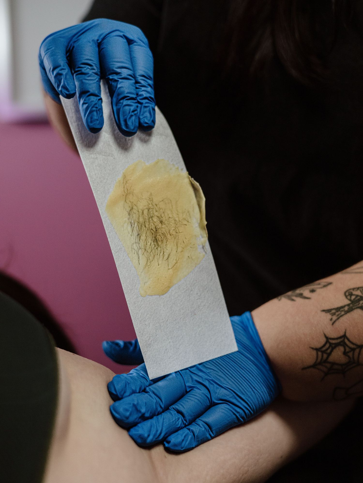 A sequence showing waxing process using blue latex gloves to apply a honey-colored wax strip to skin.