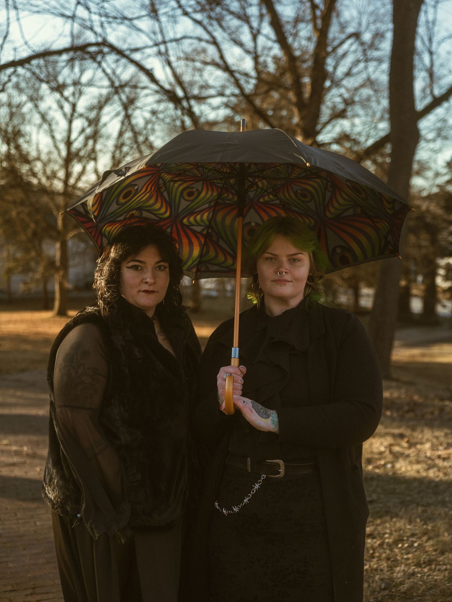 Two people in dark coats share a decorative umbrella while standing in a park during autumn.