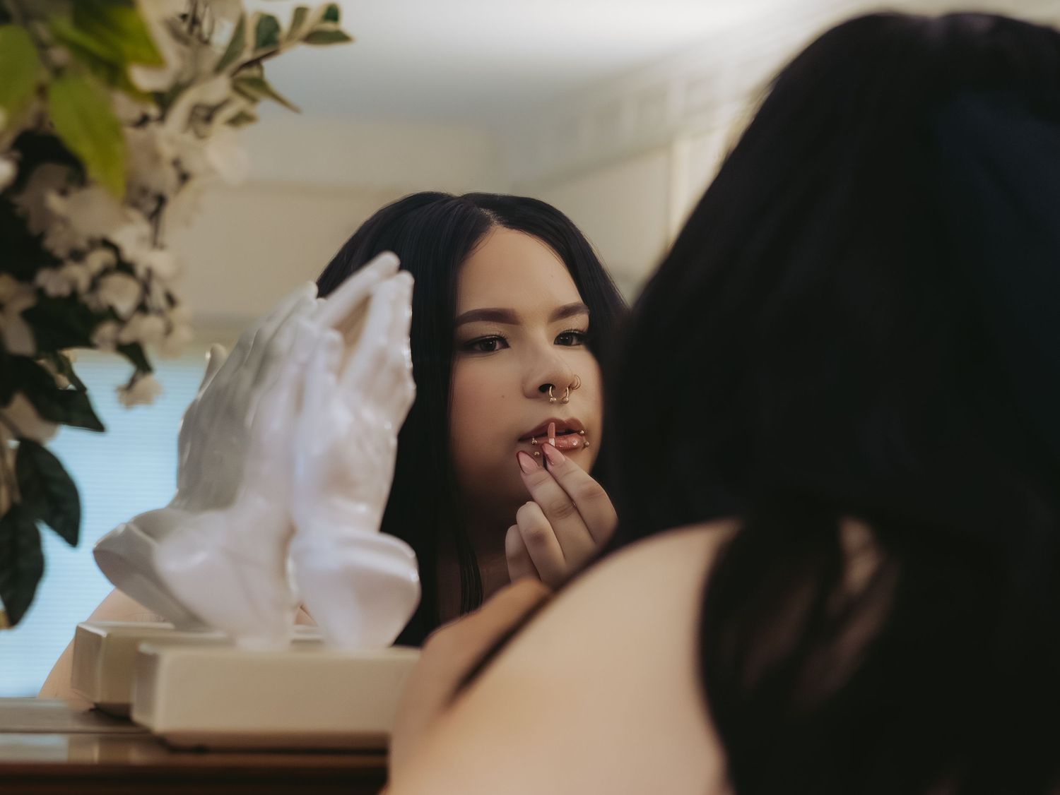 Young woman applying lipstick while looking at her reflection in a vintage mirror.
