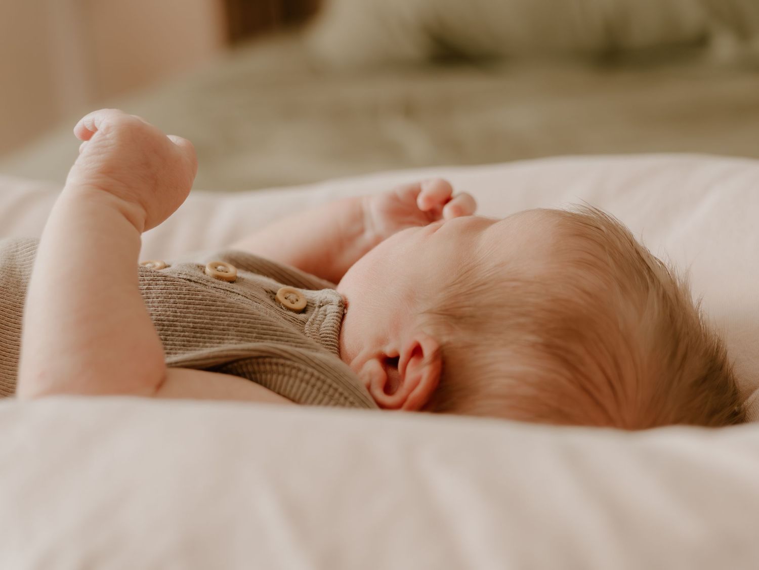 A sleeping baby lies peacefully on white bedding in warm, natural lighting.