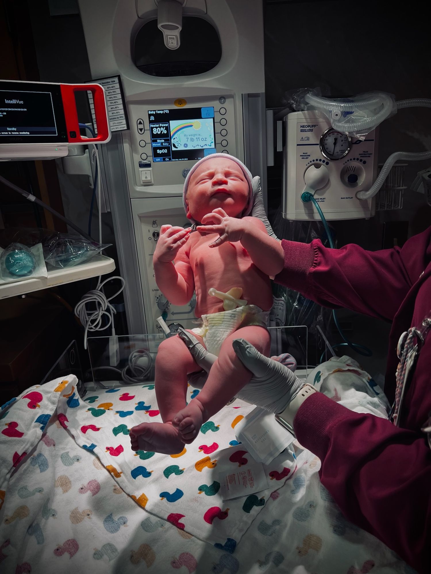 A newborn baby being examined on a colorful blanket surrounded by medical equipment.