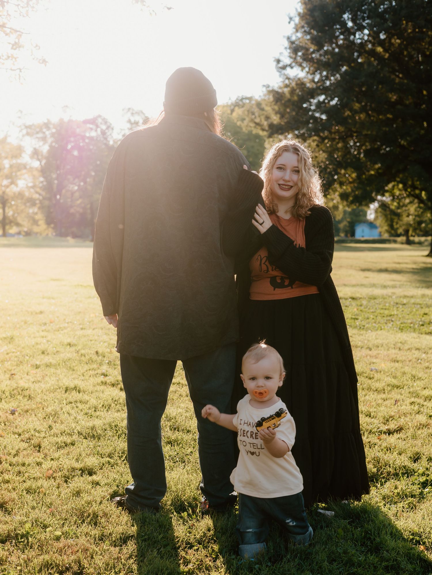 Family gathering in a sunny park with trees casting long shadows in the background.