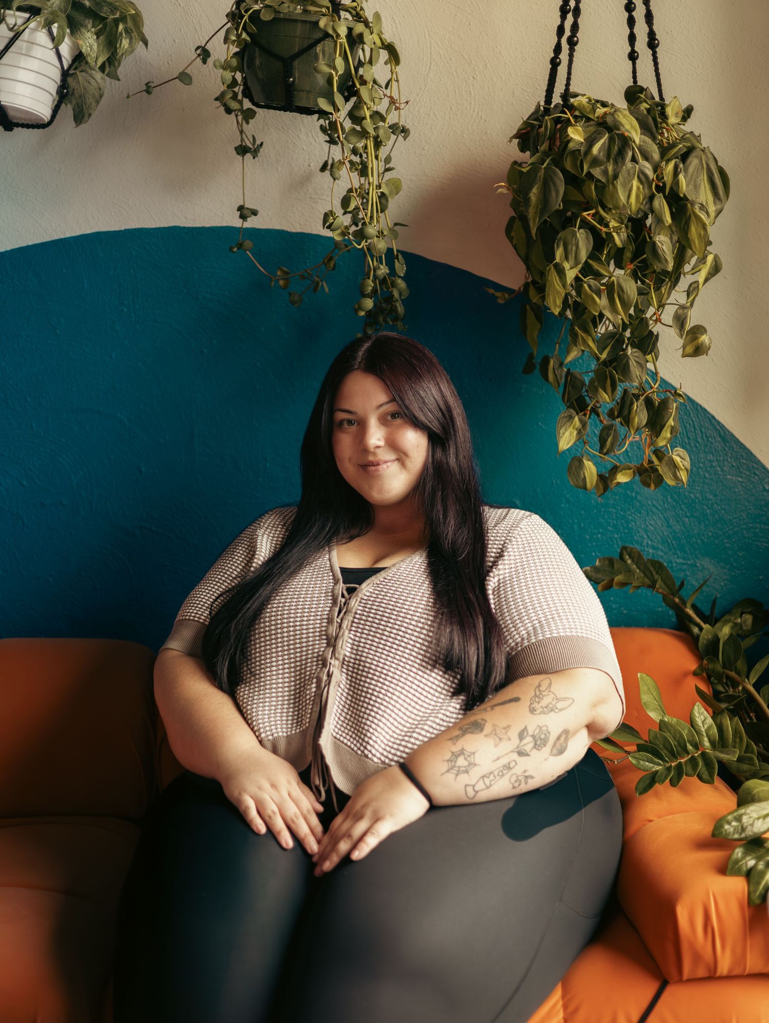 A relaxing scene with hanging plants and a teal curved couch with orange accent pillows.