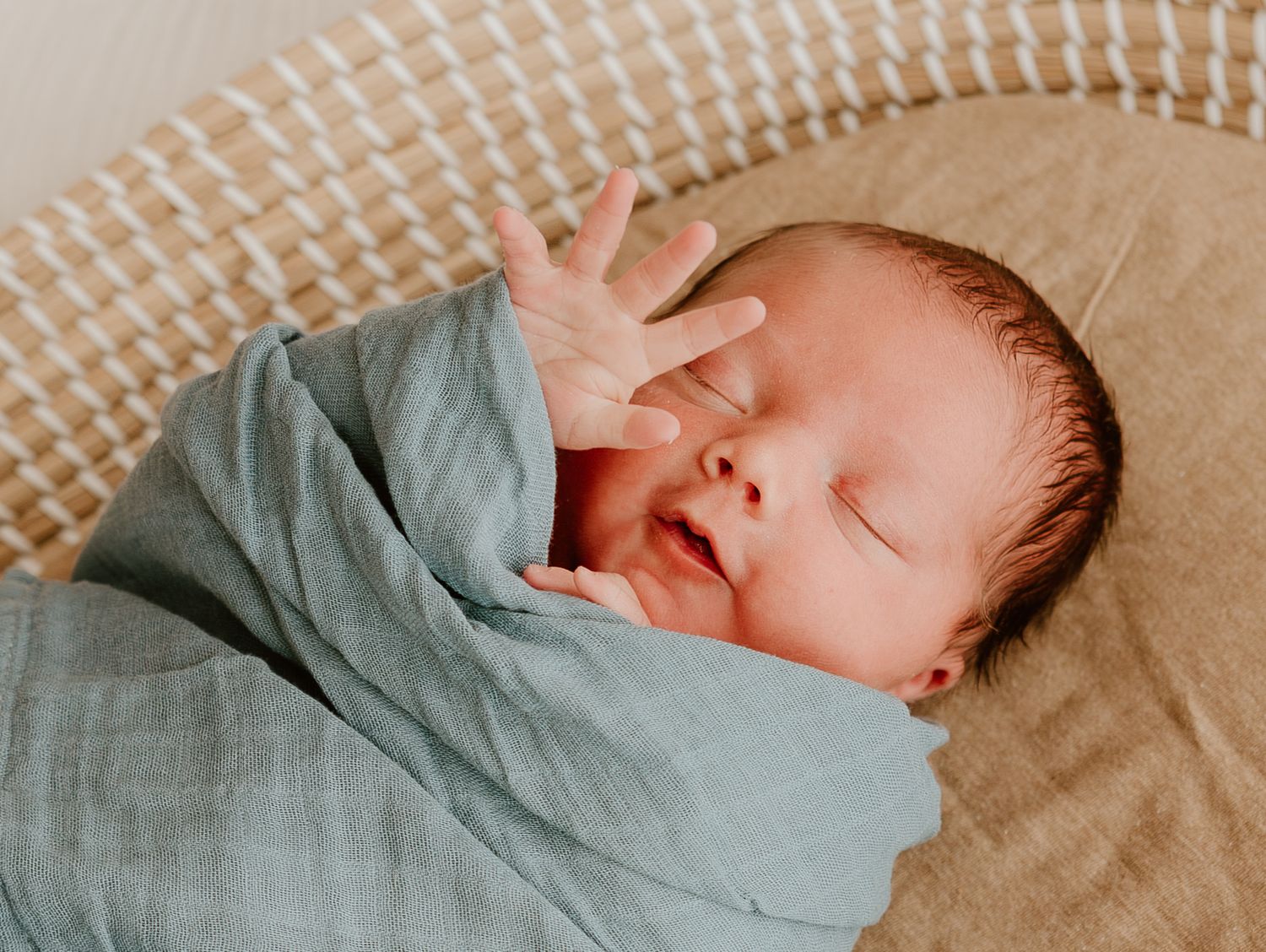 A sleeping newborn baby wrapped in a soft mint green swaddle blanket.