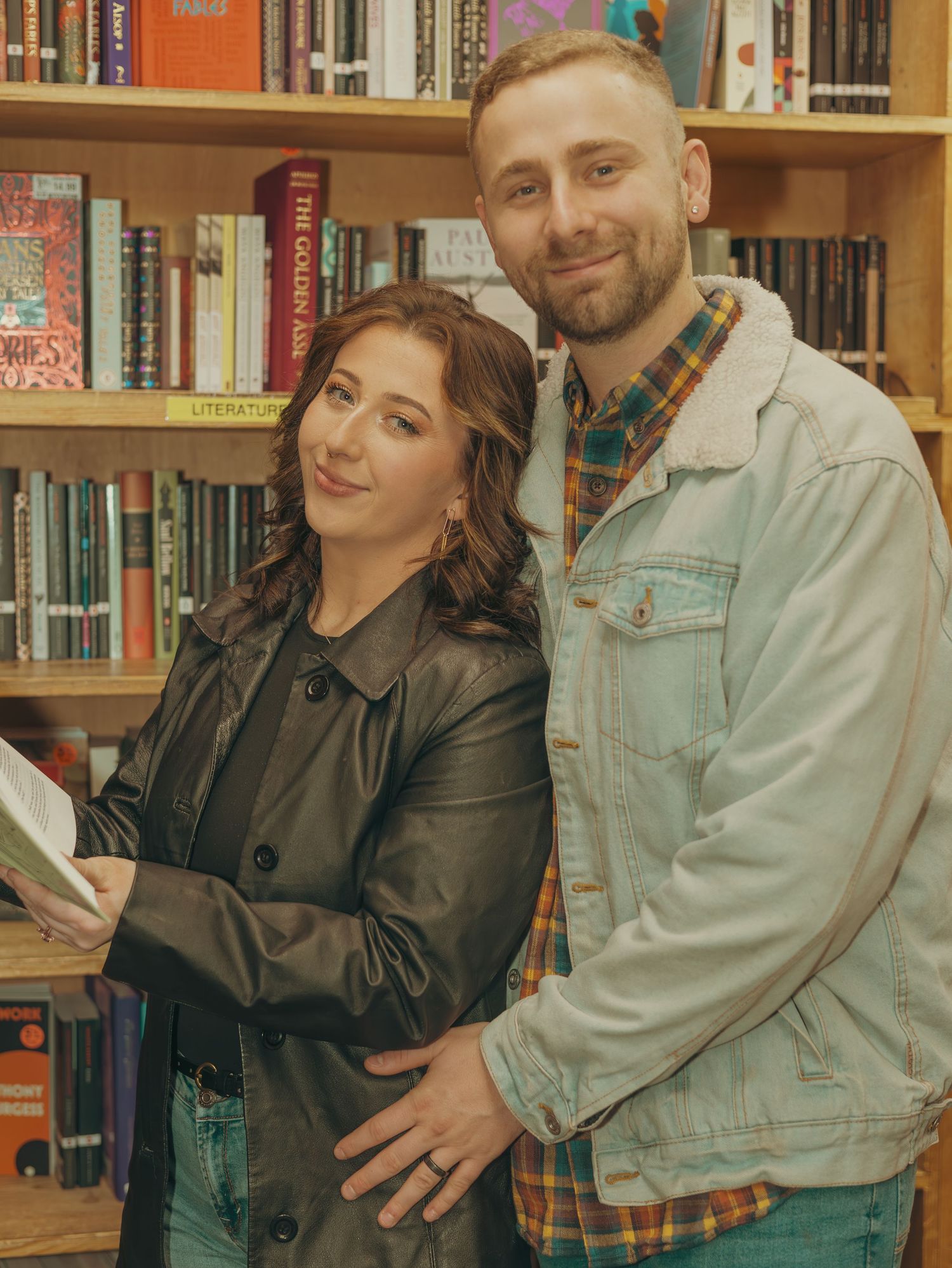 A couple poses together in front of a library bookshelf, creating a cozy and intimate atmosphere.