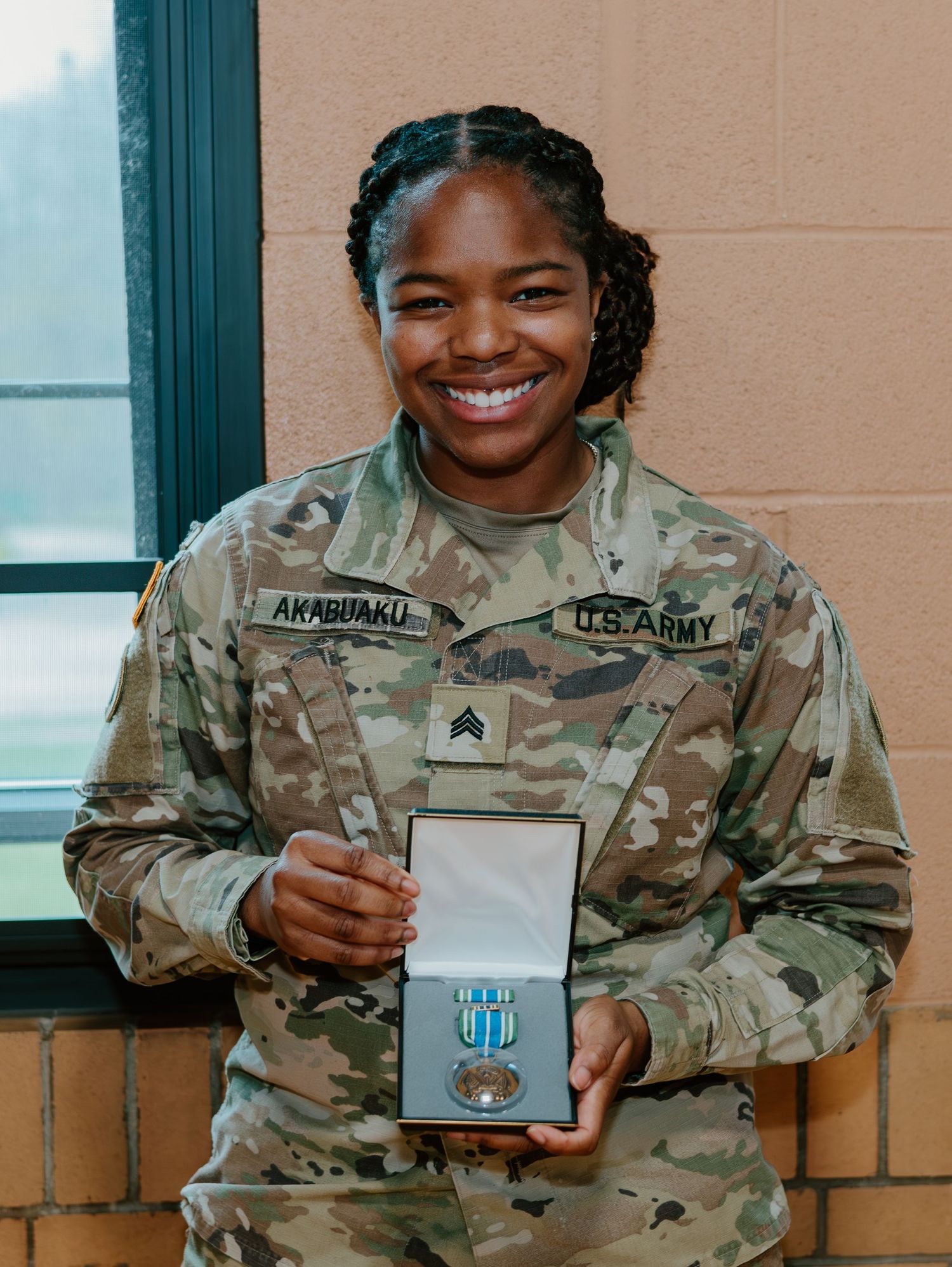 A service member in US Army camouflage uniform displays a medal case with an award inside.
