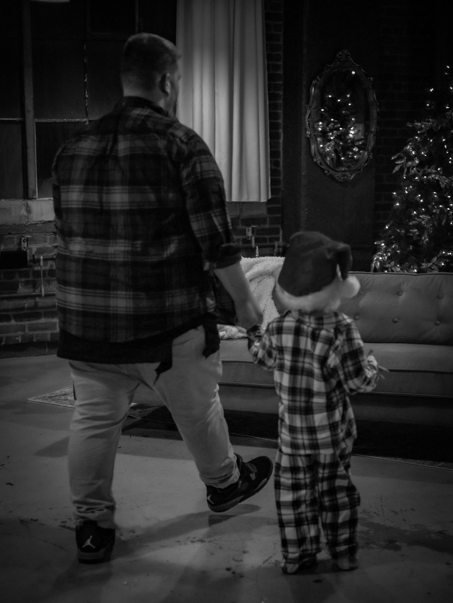 A figure in plaid holds hands with small child in matching pajamas beside Christmas decorations.