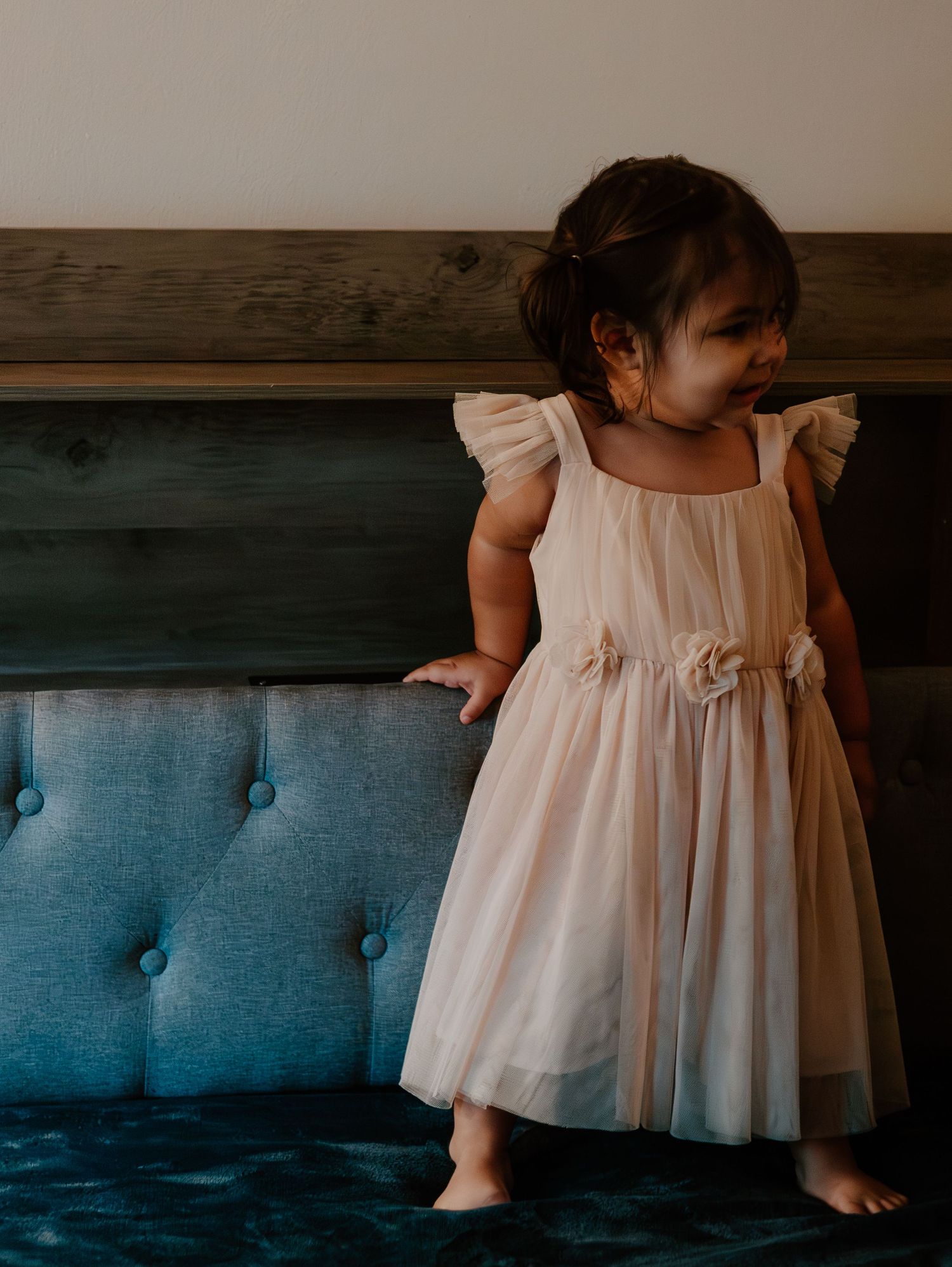 White-dressed toddler standing on a blue tufted couch in a series of candid shots.