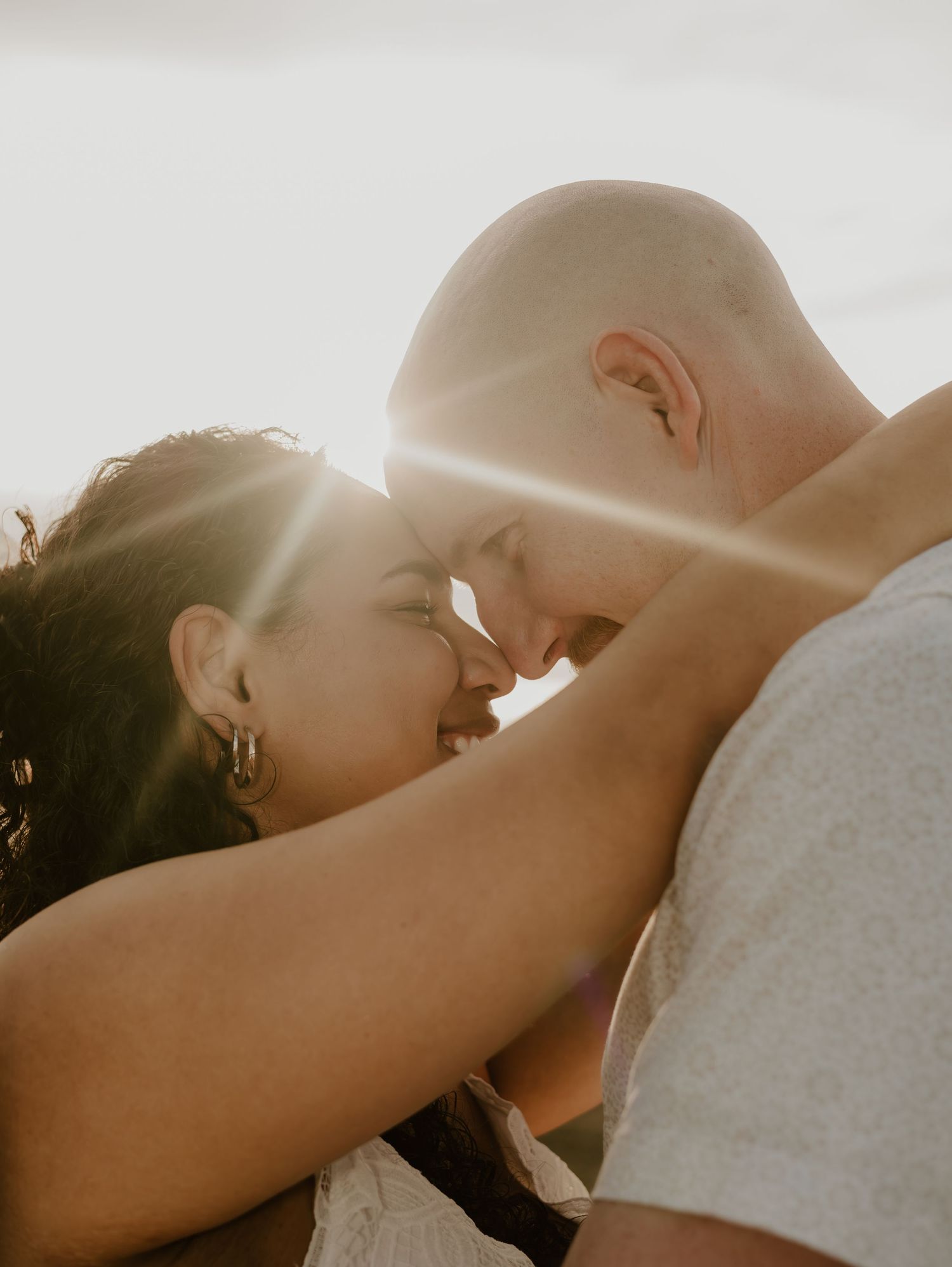 Intimate silhouette of a couple sharing a tender kiss against sunlit backdrop.