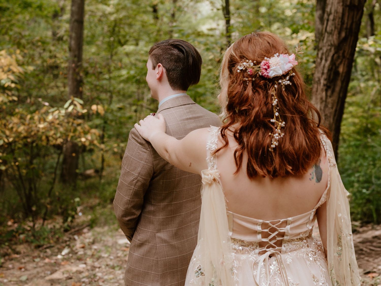 A romantic wedding couple walks hand in hand through a sunlit forest path surrounded by lush greenery.
