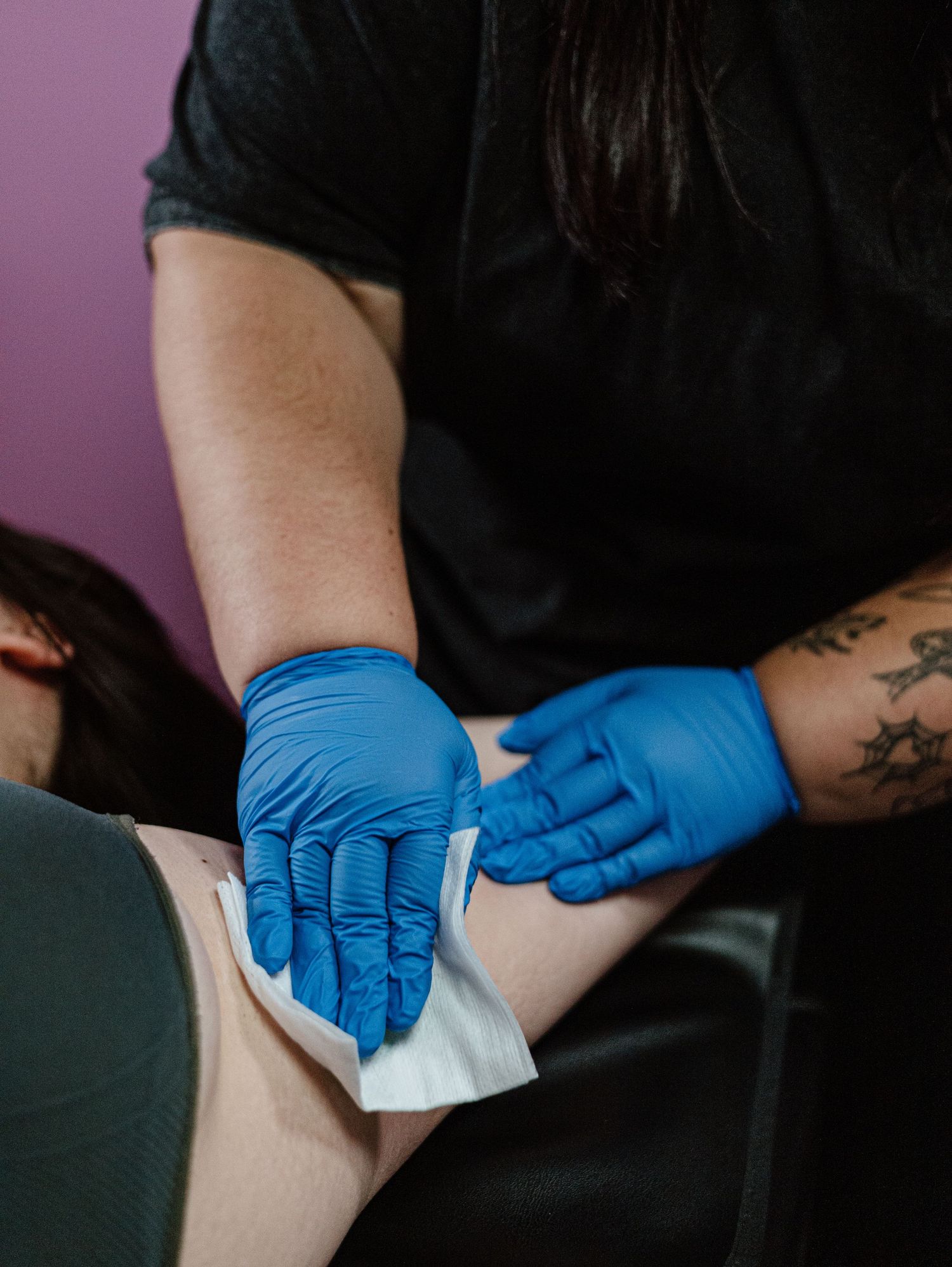 Healthcare professional wearing blue latex gloves performs medical procedure with white gauze against purple background.