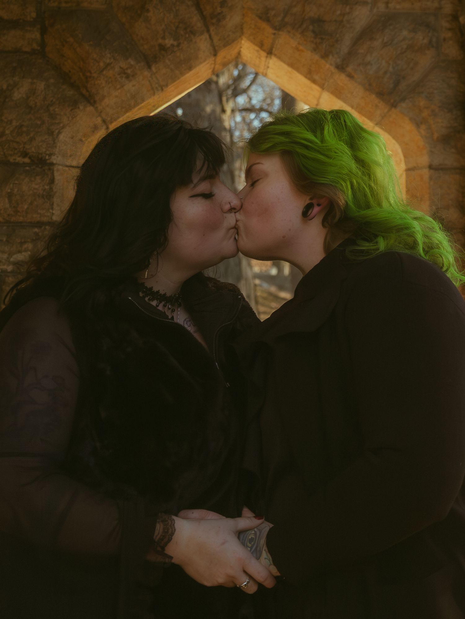 Two figures share a romantic moment in a dimly lit stone archway, one with striking green hair.