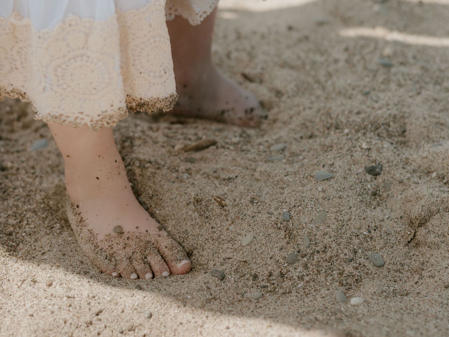 Close-up view of bare feet and sandals arranged on sandy beach ground.