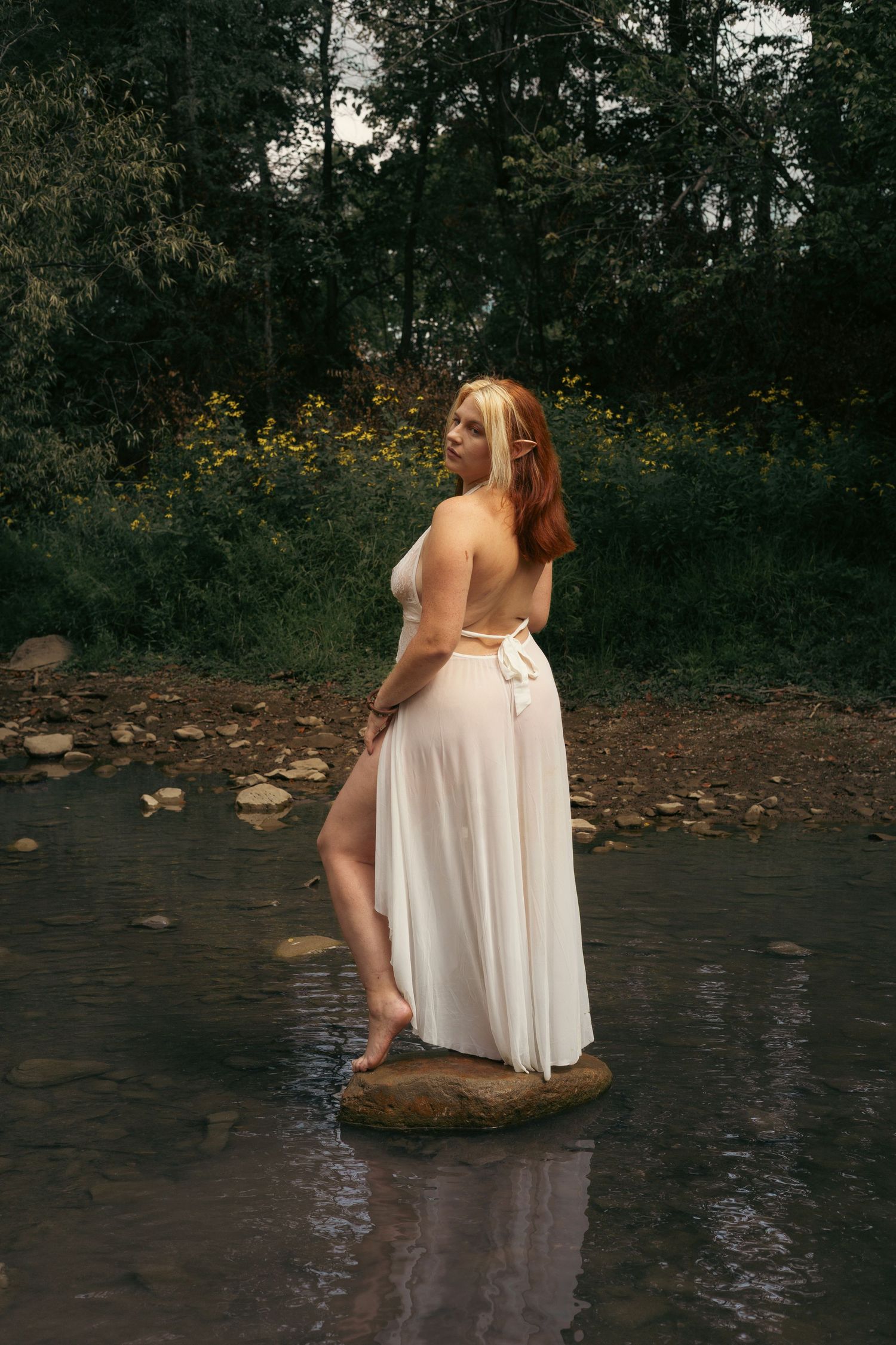 A sequence of photos showing a person in a flowing white dress sitting gracefully by a stream in a wooded setting.