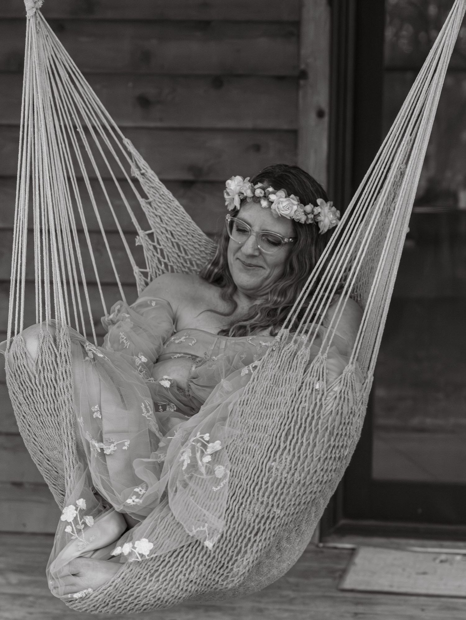 A dreamy black and white photo of a bride wearing a flower crown while relaxing in a hammock.