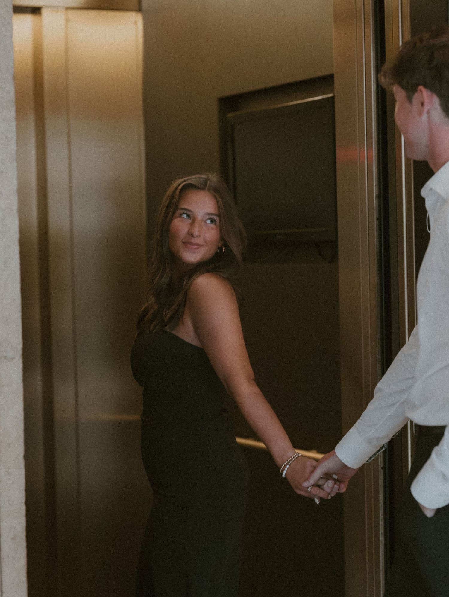 A stylish couple shares tender moments in a dimly lit hallway setting.