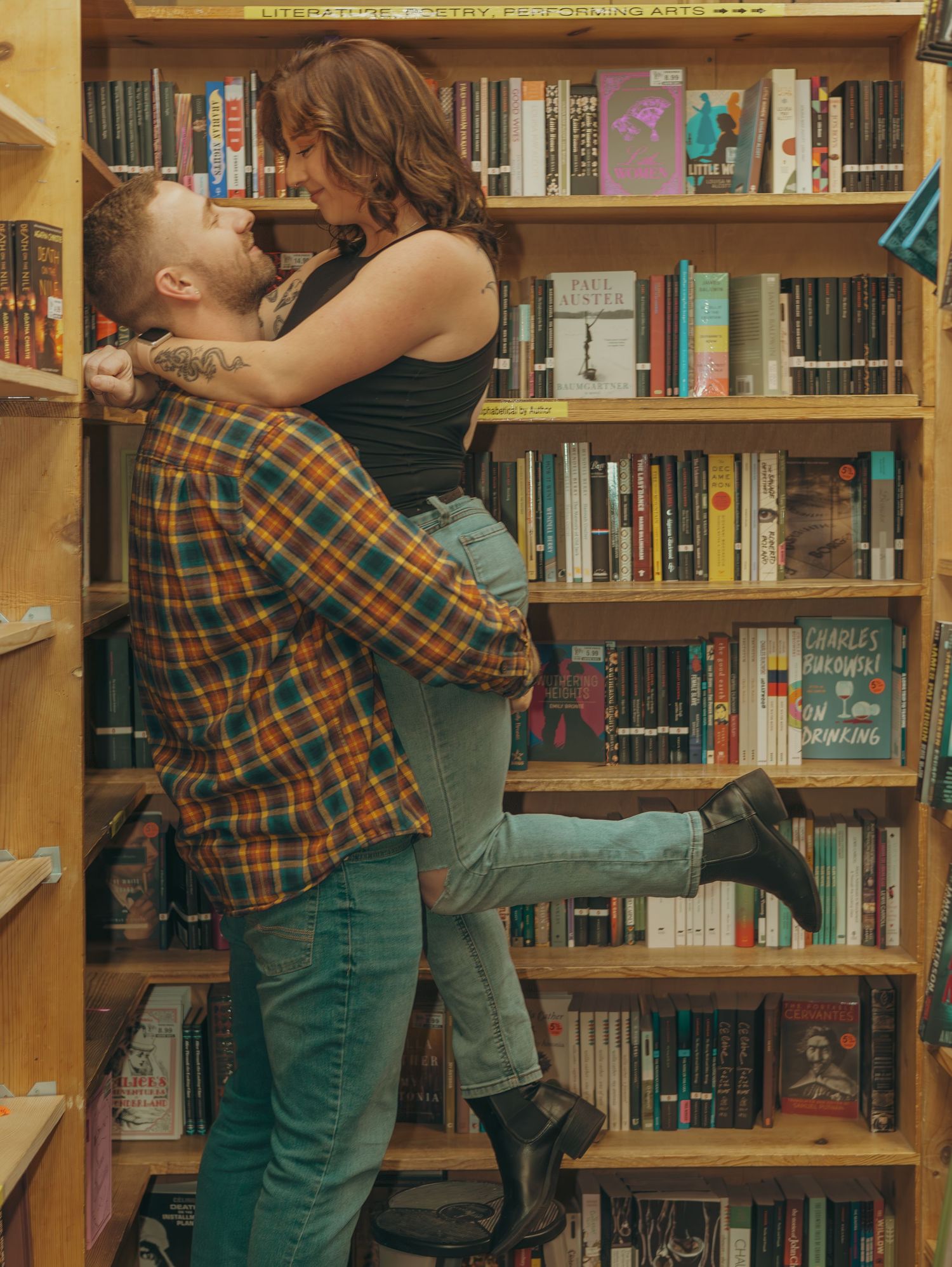 A couple embraces romantically between bookshelves in a cozy library setting.