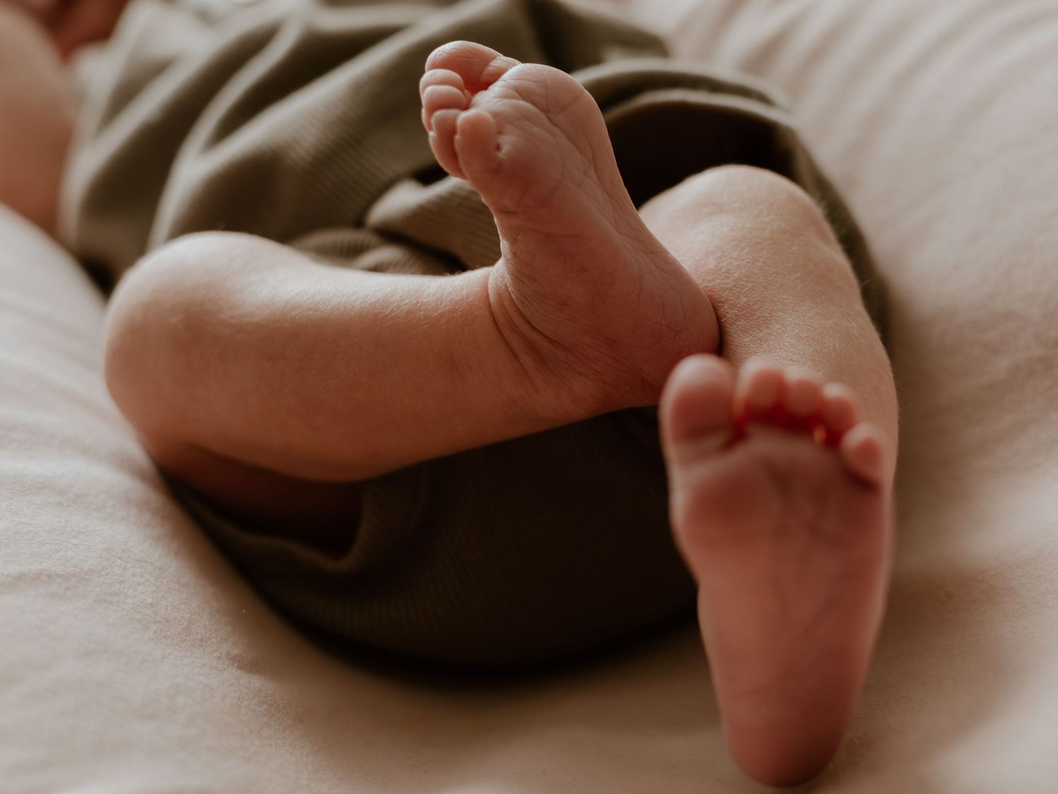 Newborn baby feet gently resting on cozy brown knit fabric in natural lighting.