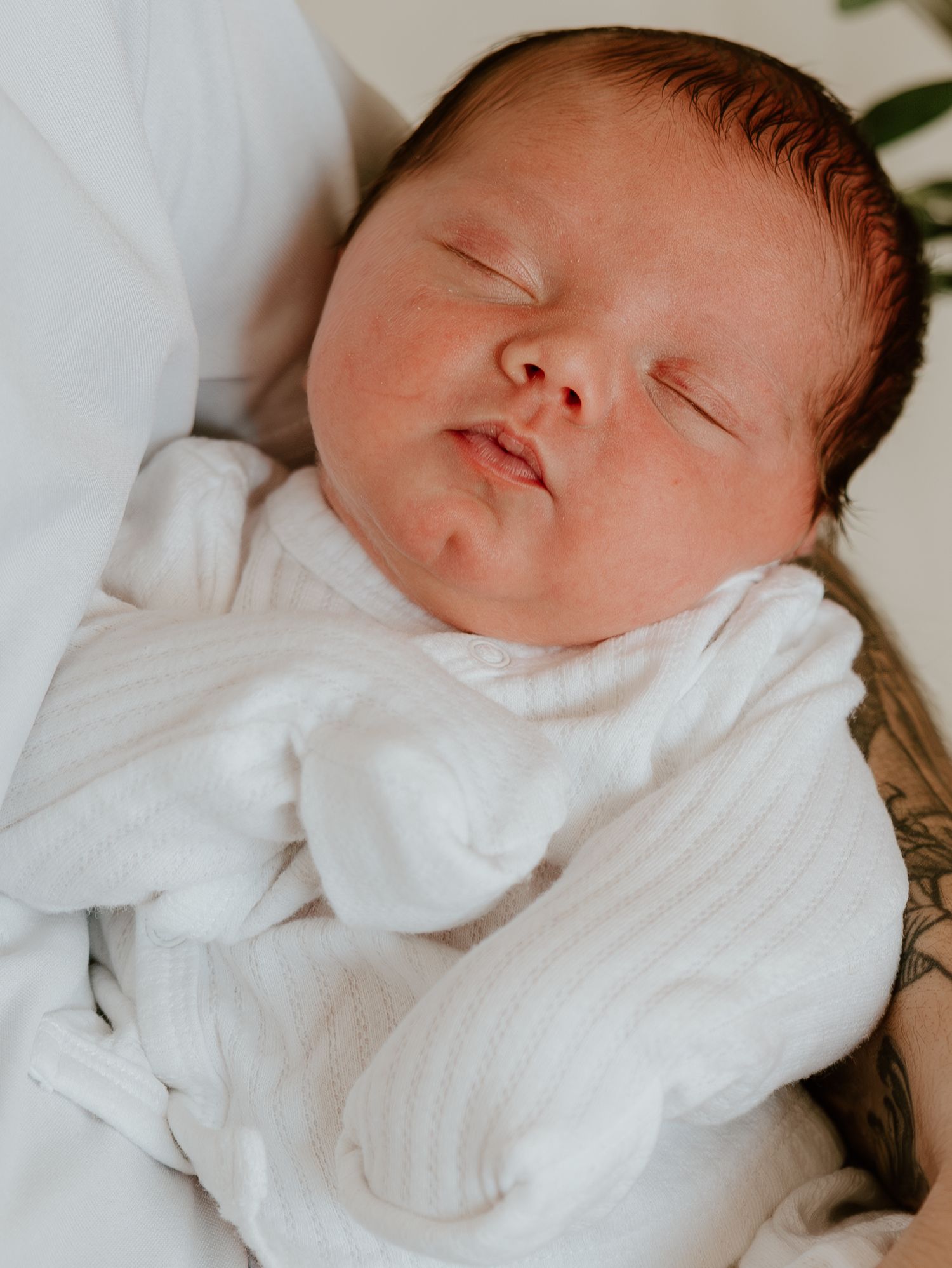 Sleeping infant wrapped in white swaddle blanket resting on soft bedding.