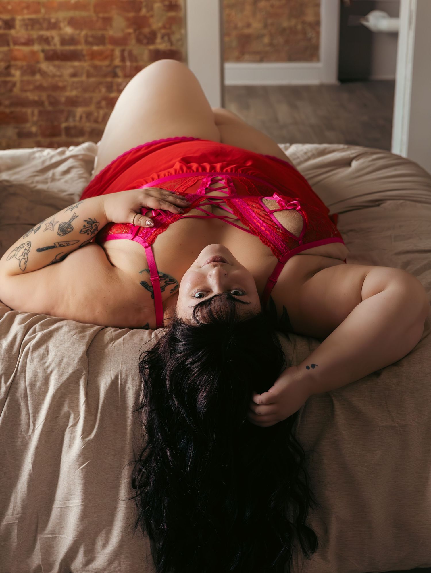 Intimate boudoir portrait in red lingerie against brick wall backdrop.