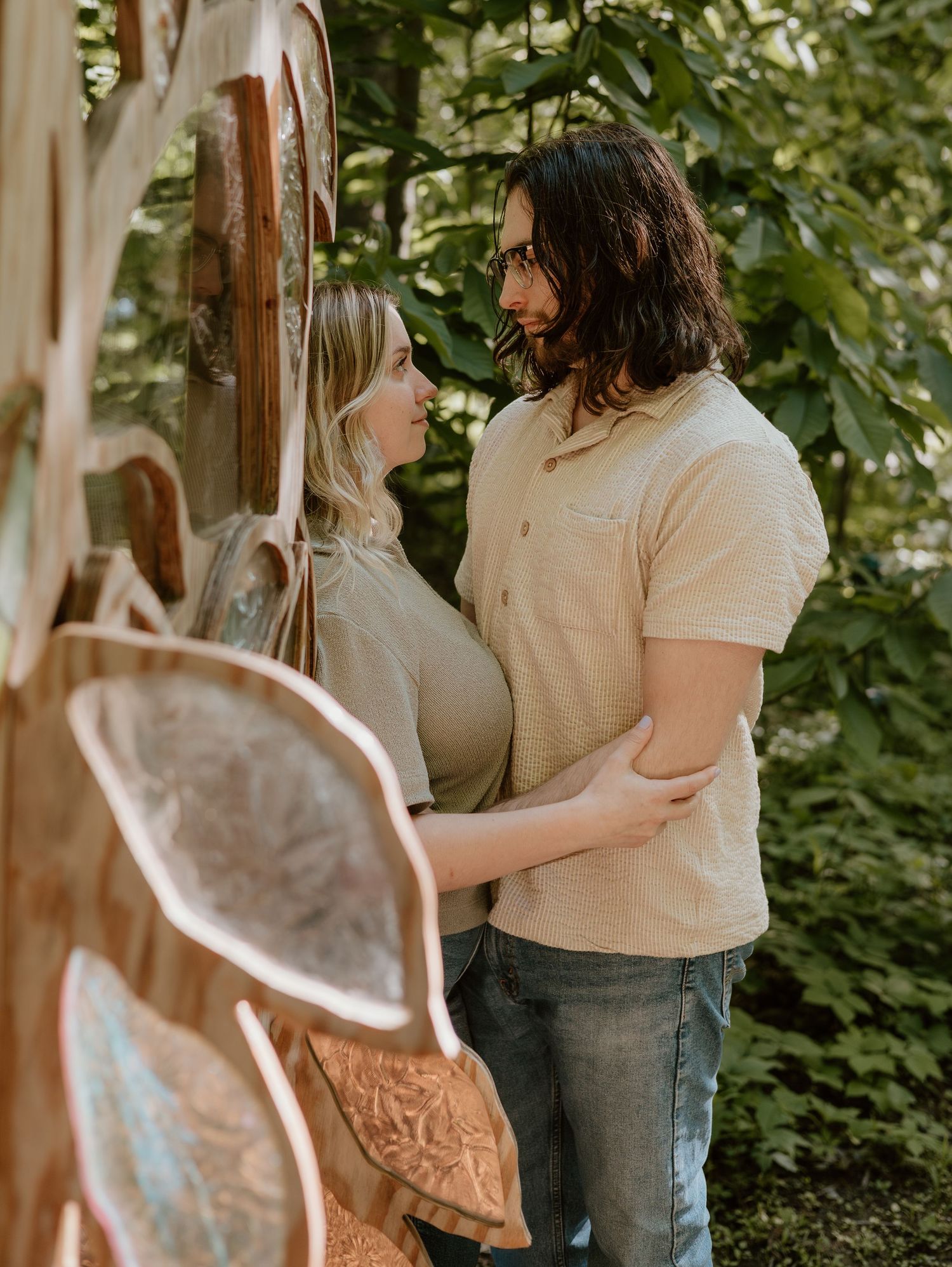 A tender embrace between two people in casual attire standing in a lush garden setting.
