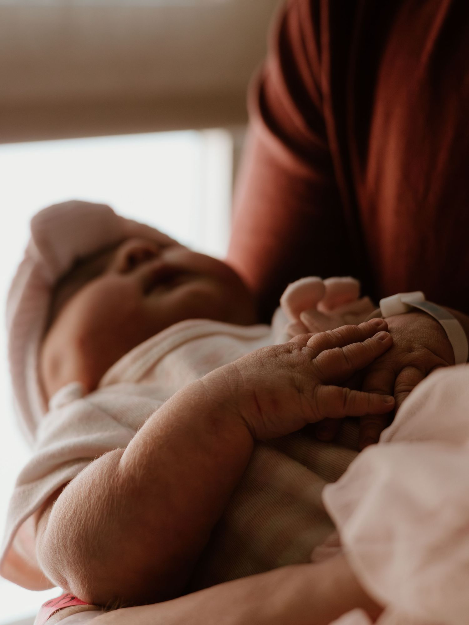 A series of tender close-up shots showing gentle hands cradling a sleeping newborn baby wrapped in white.