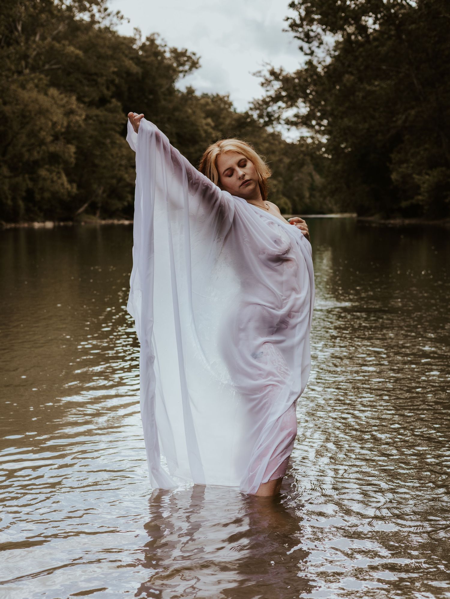 A series of artistic shots showing a figure in white fabric flowing gracefully in lake water at dusk.