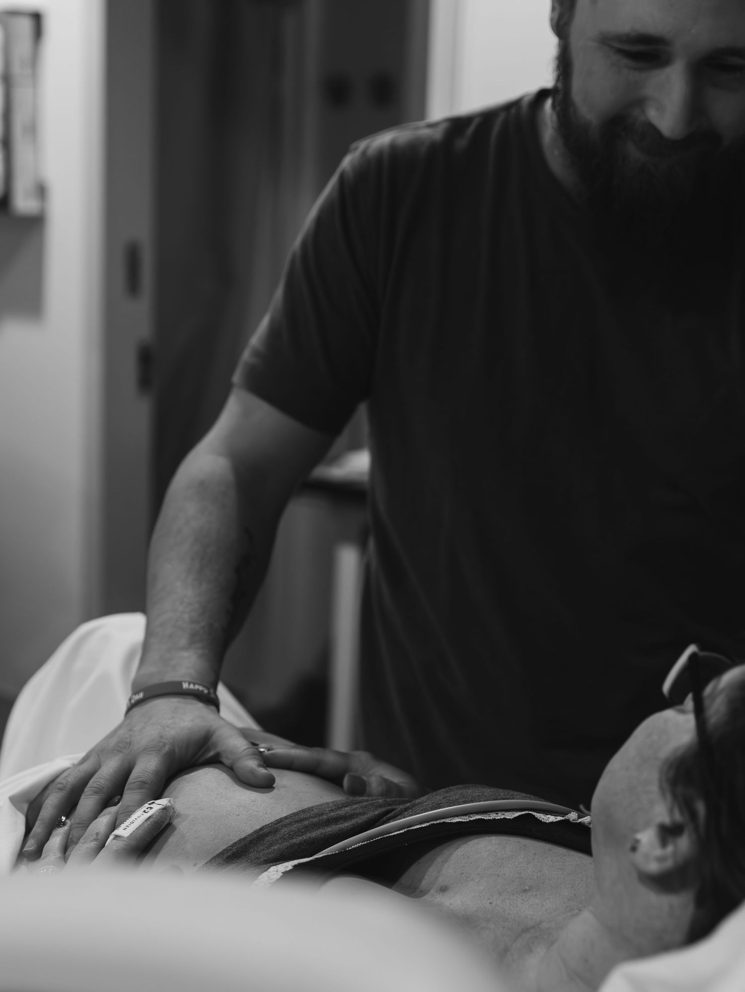 Black and white photo of a bearded man gently supporting a pregnant woman lying down during labor.