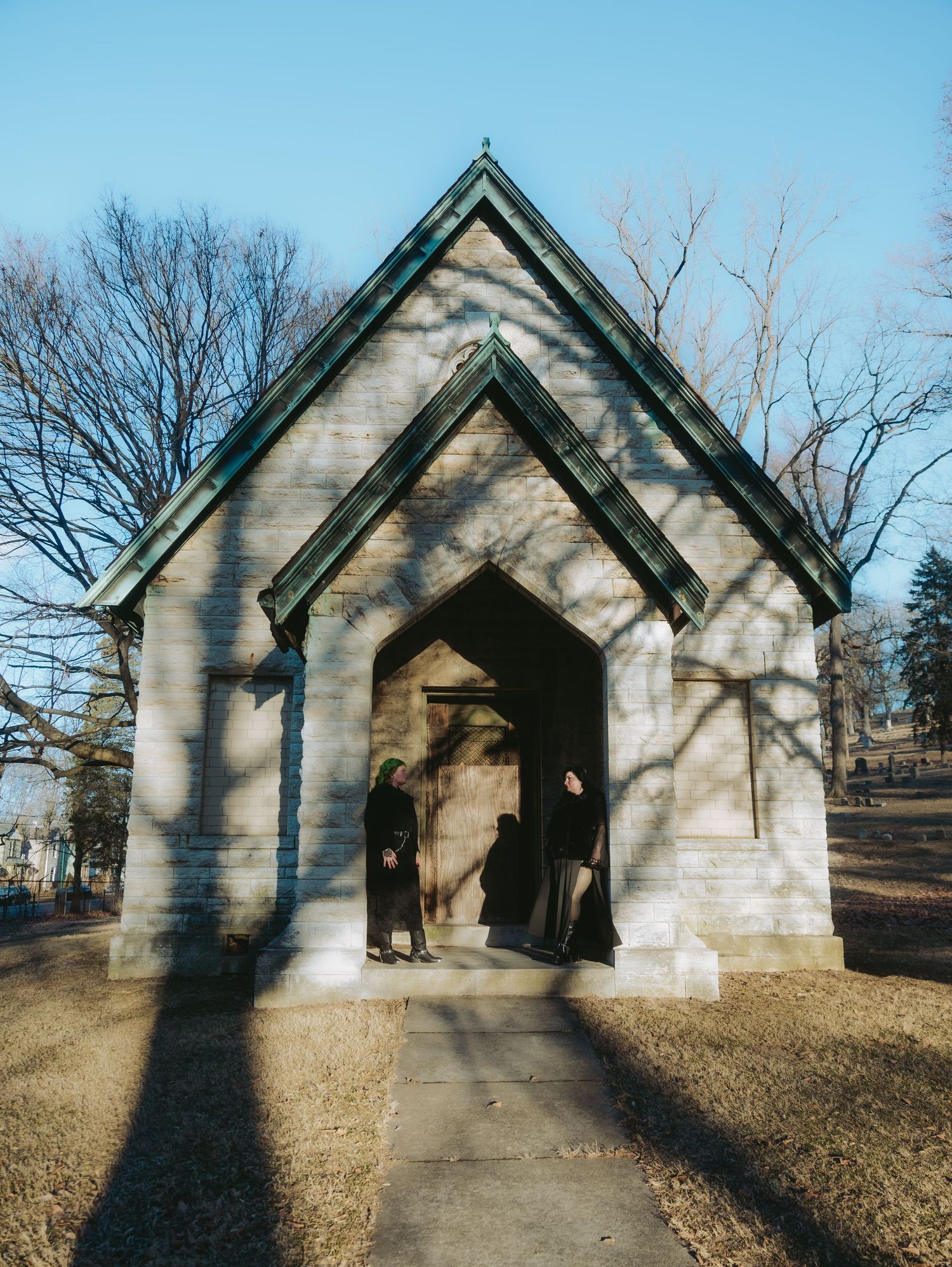 Two figures stand in the doorway of a small white gothic chapel on a winter day.