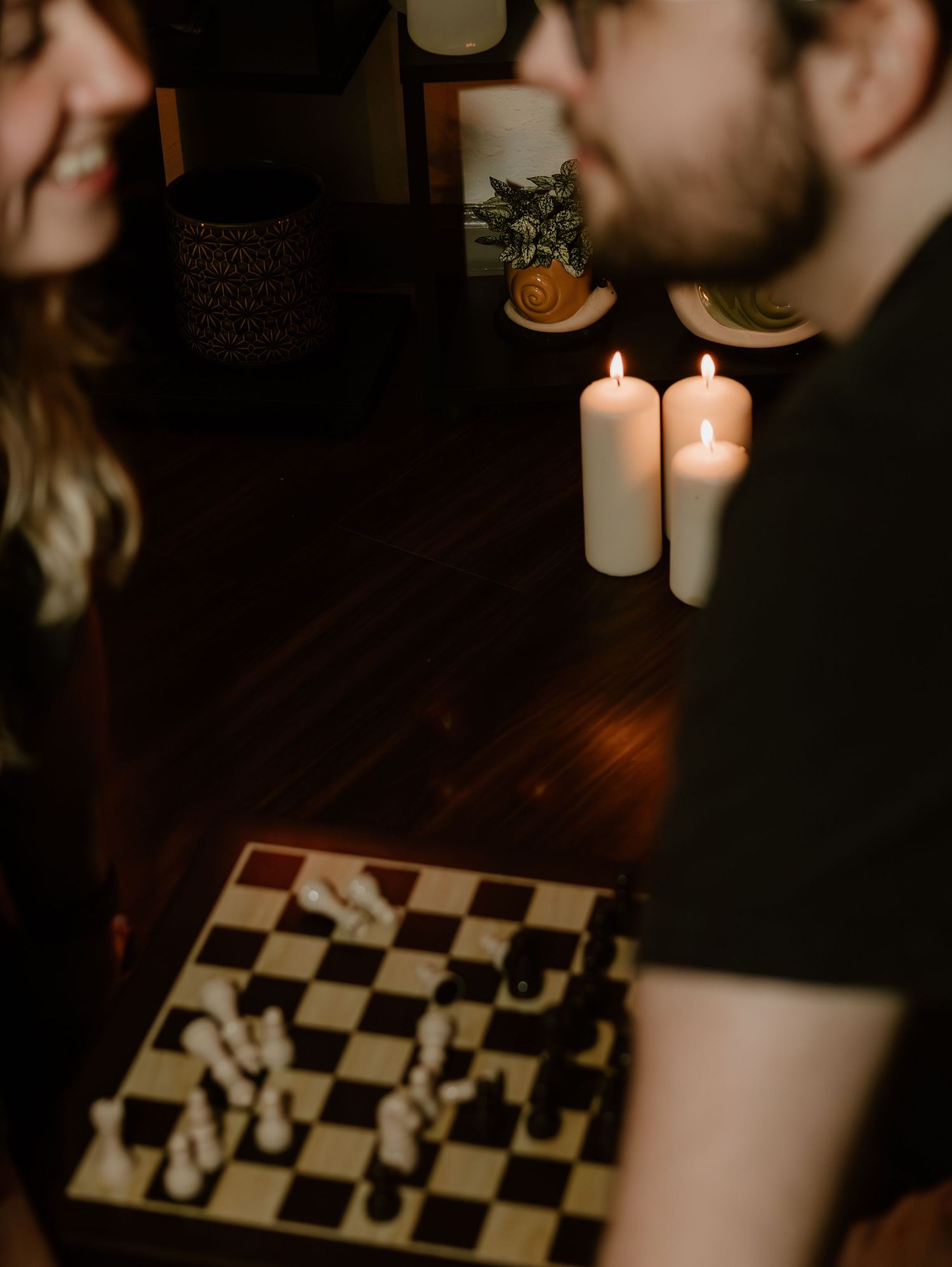 A dark and moody chess game setup with white candles burning beside the board, creating a dramatic atmosphere.