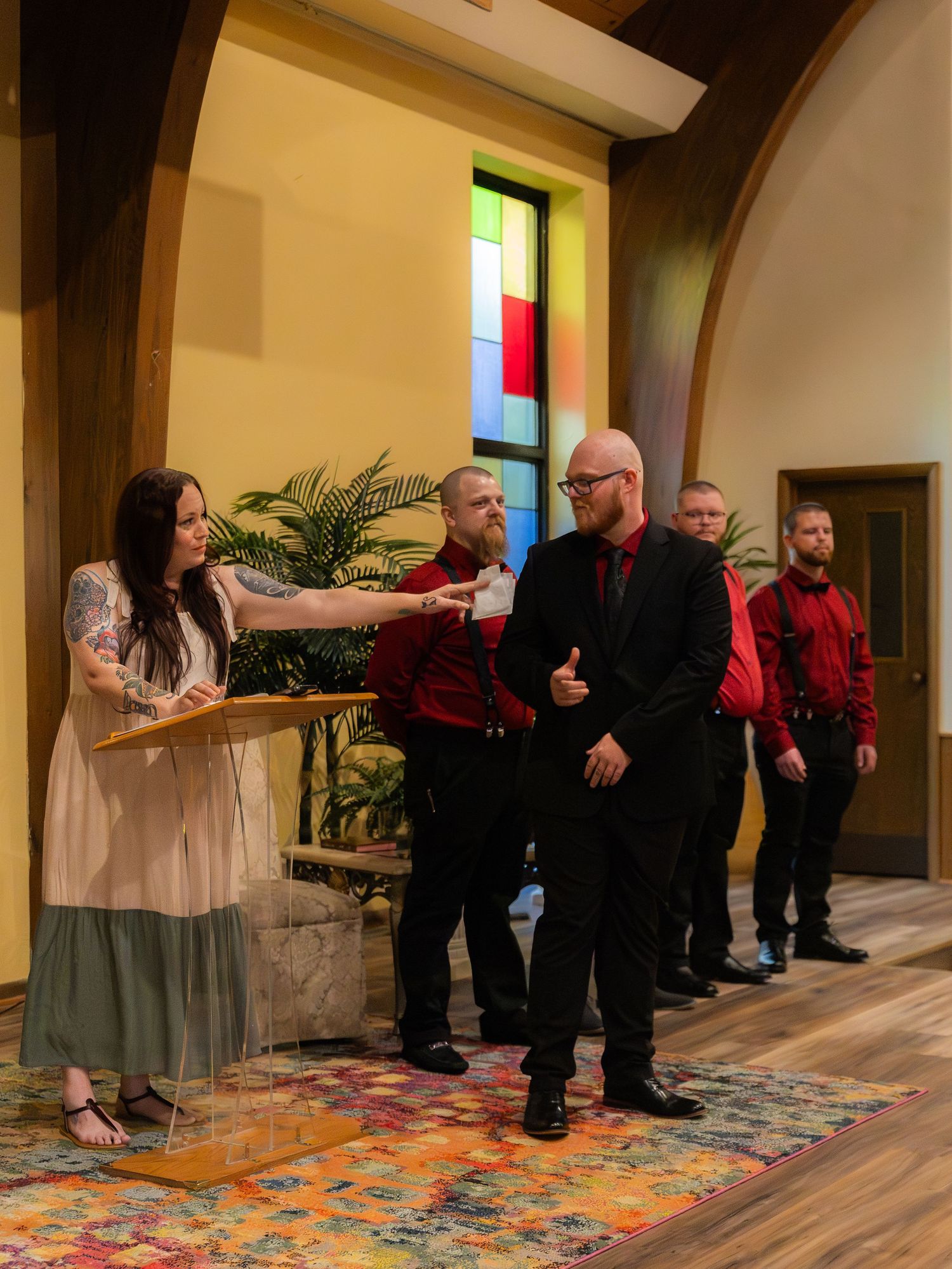 Woman at podium shaking hands with bald man in black suit, four men in red and black attire stand in church.