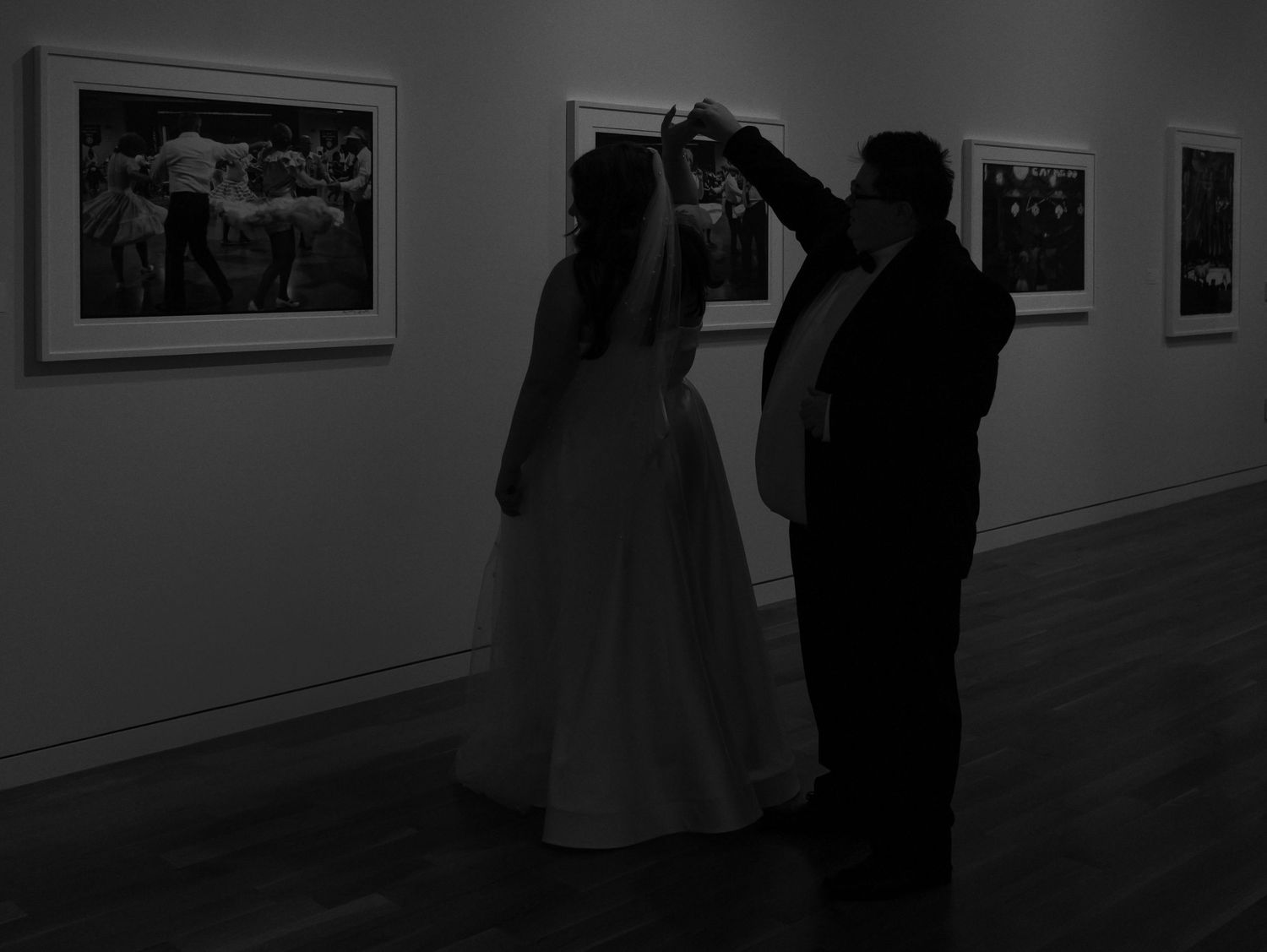 Silhouettes of people viewing artwork in a dimly lit gallery space.