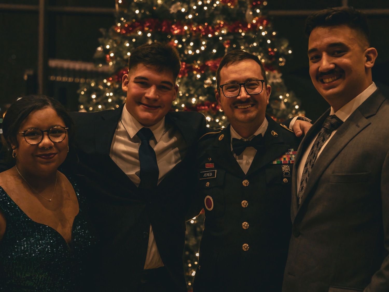 Friends pose together at a holiday party in front of a sparkling Christmas tree.